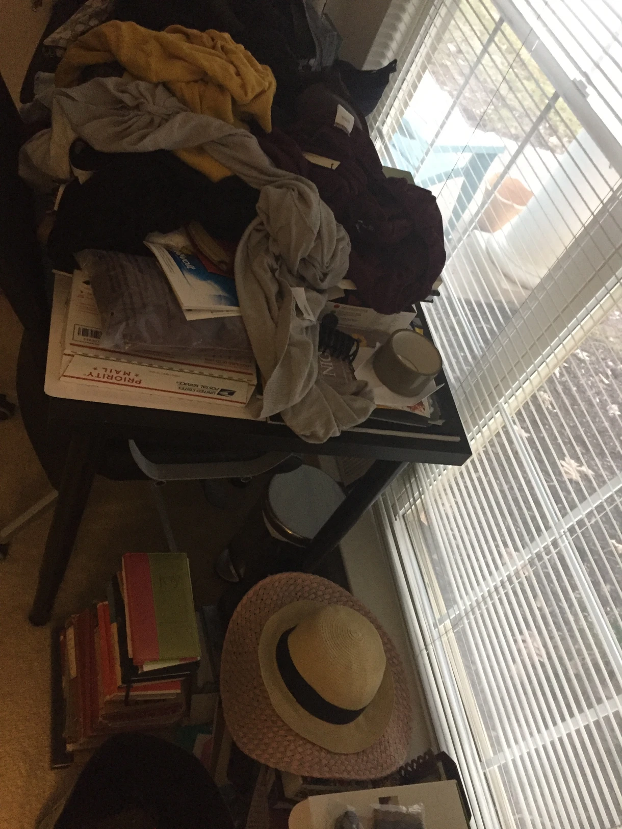 Cluttered bedroom corner with clothes, books, and items stacked on a small table.