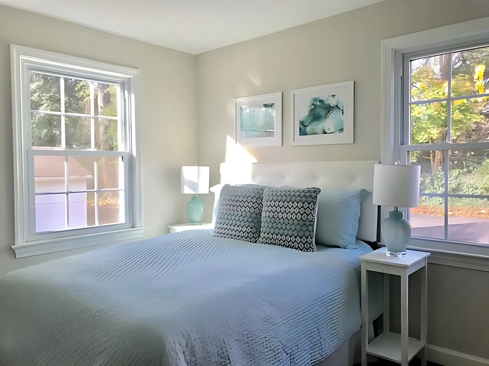 Minimal bedroom with bed, bedside table, and natural light from two windows.