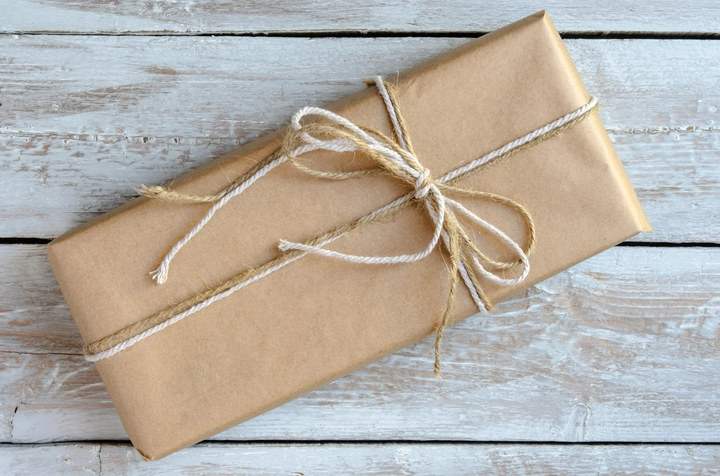 Wrapped gift in brown paper with string on a wooden surface, representing giving and donation.