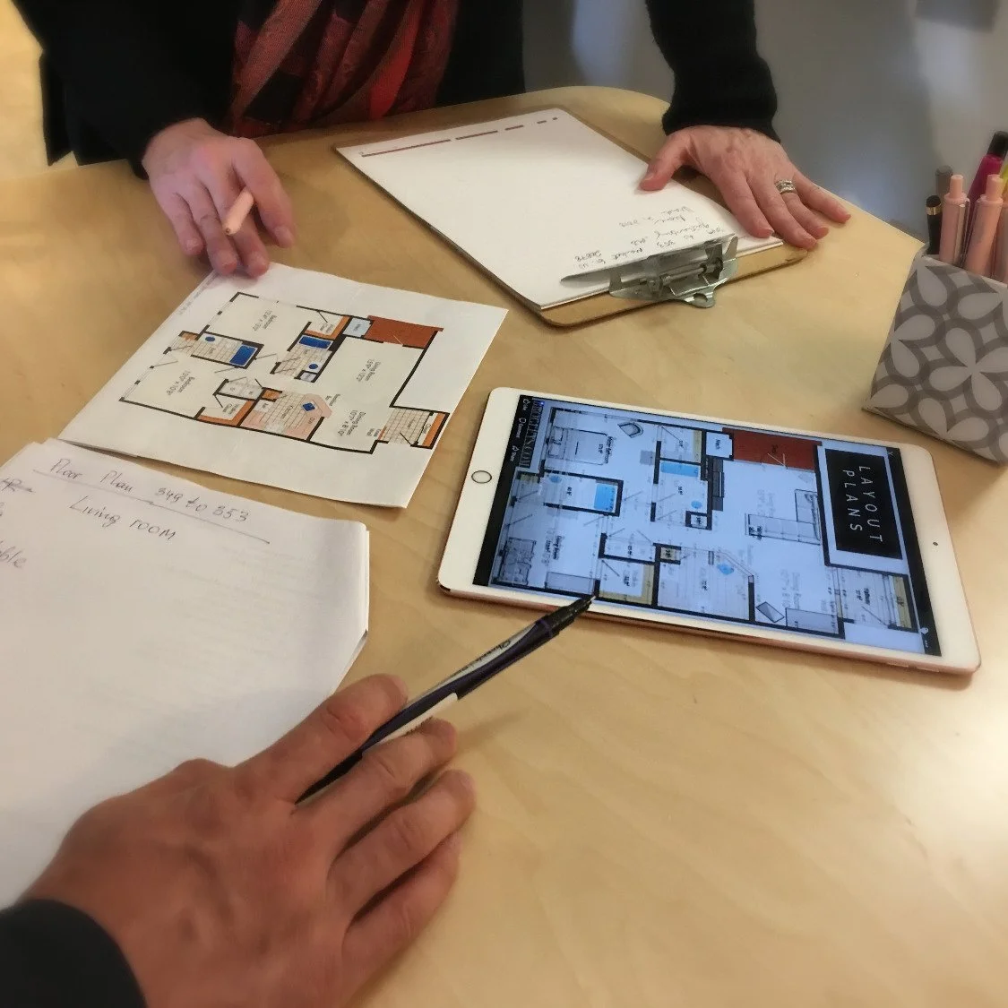 Close-up of hands planning layout with tablet and documents on a table.