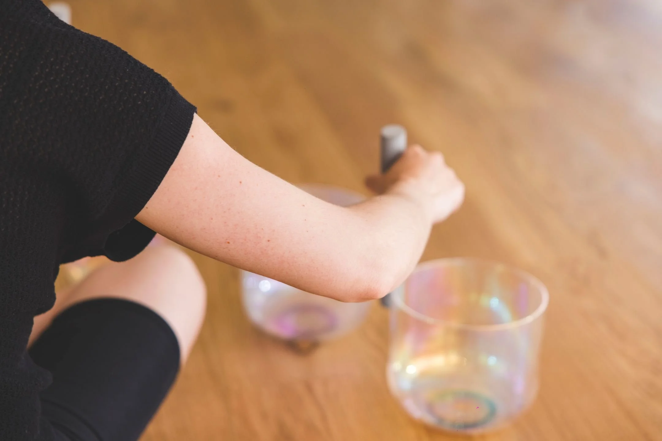Formation de Yoga Nidra 50h, module 2 sur la transmission. La professeure joue aux bols de cristal, mailloche dans sa main droite, assise avec une tenue noire directement sur le sol en parquet.