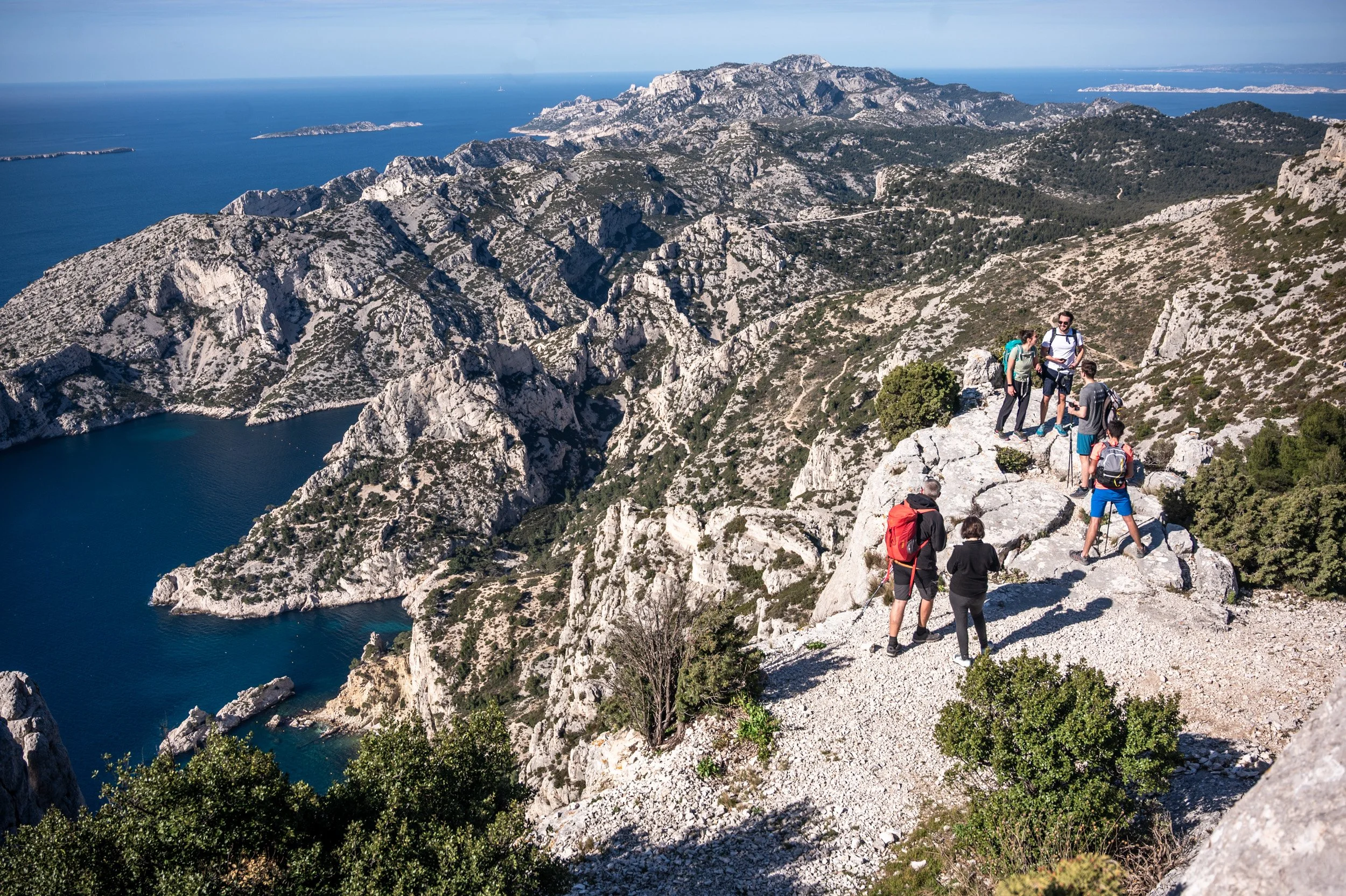 Groupe de randonneurs sur un sentier rocheux surplombant la mer, avec montagnes et îles en arrière-plan