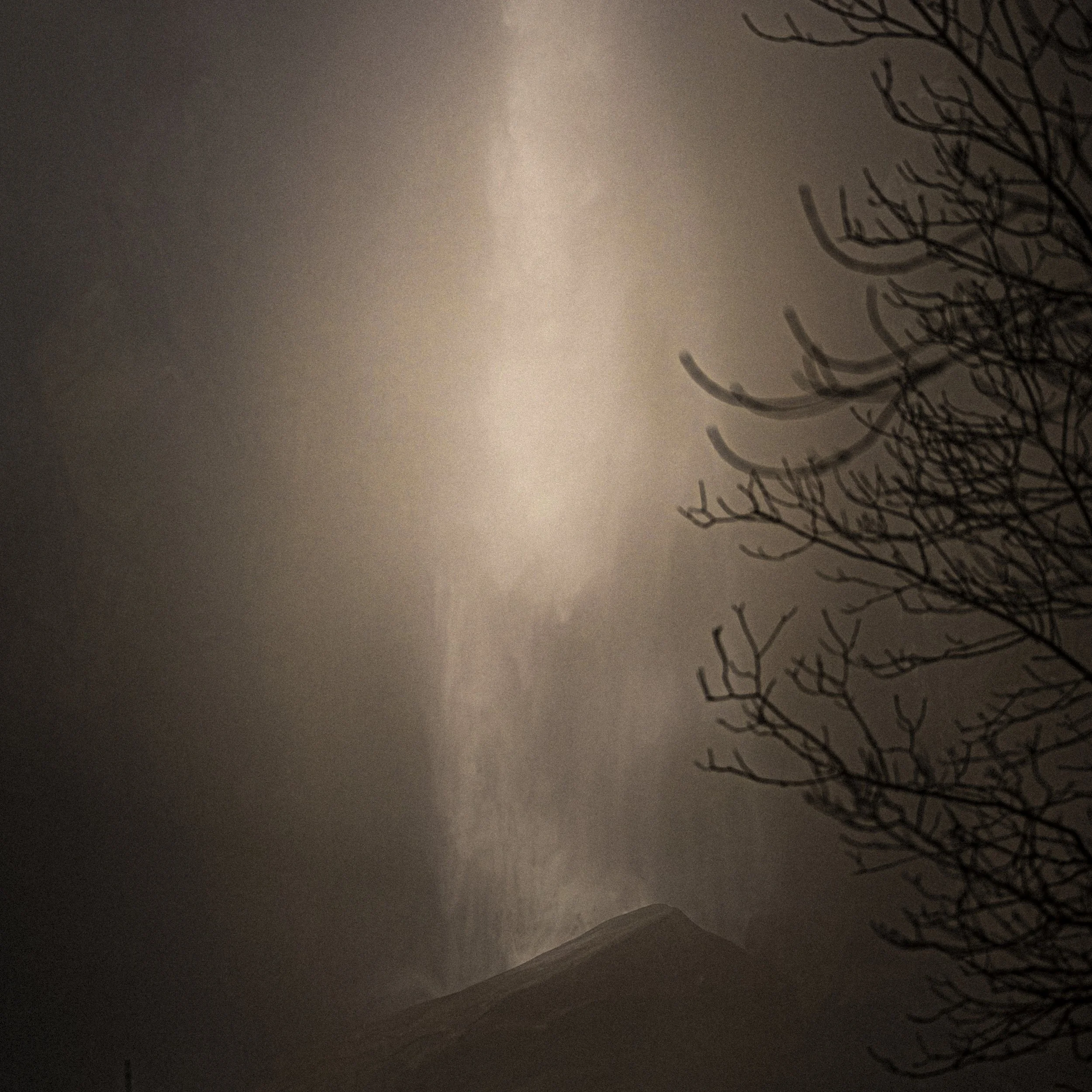 Une vue nocturne d'une montagne avec des nuages sombres et un arbre sans feuilles à droite.