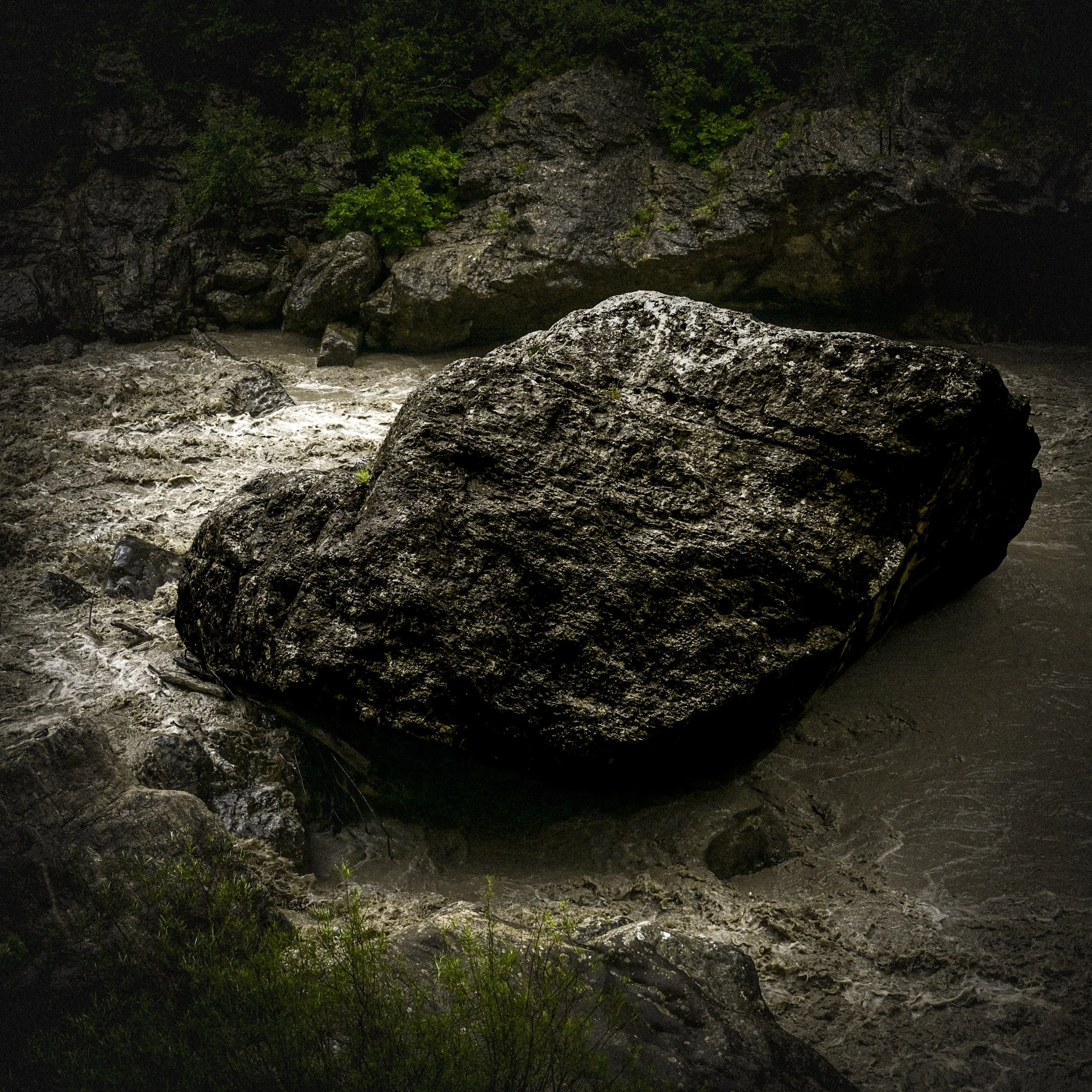 Gros rocher dans une rivière agitée entourée de végétation verte.