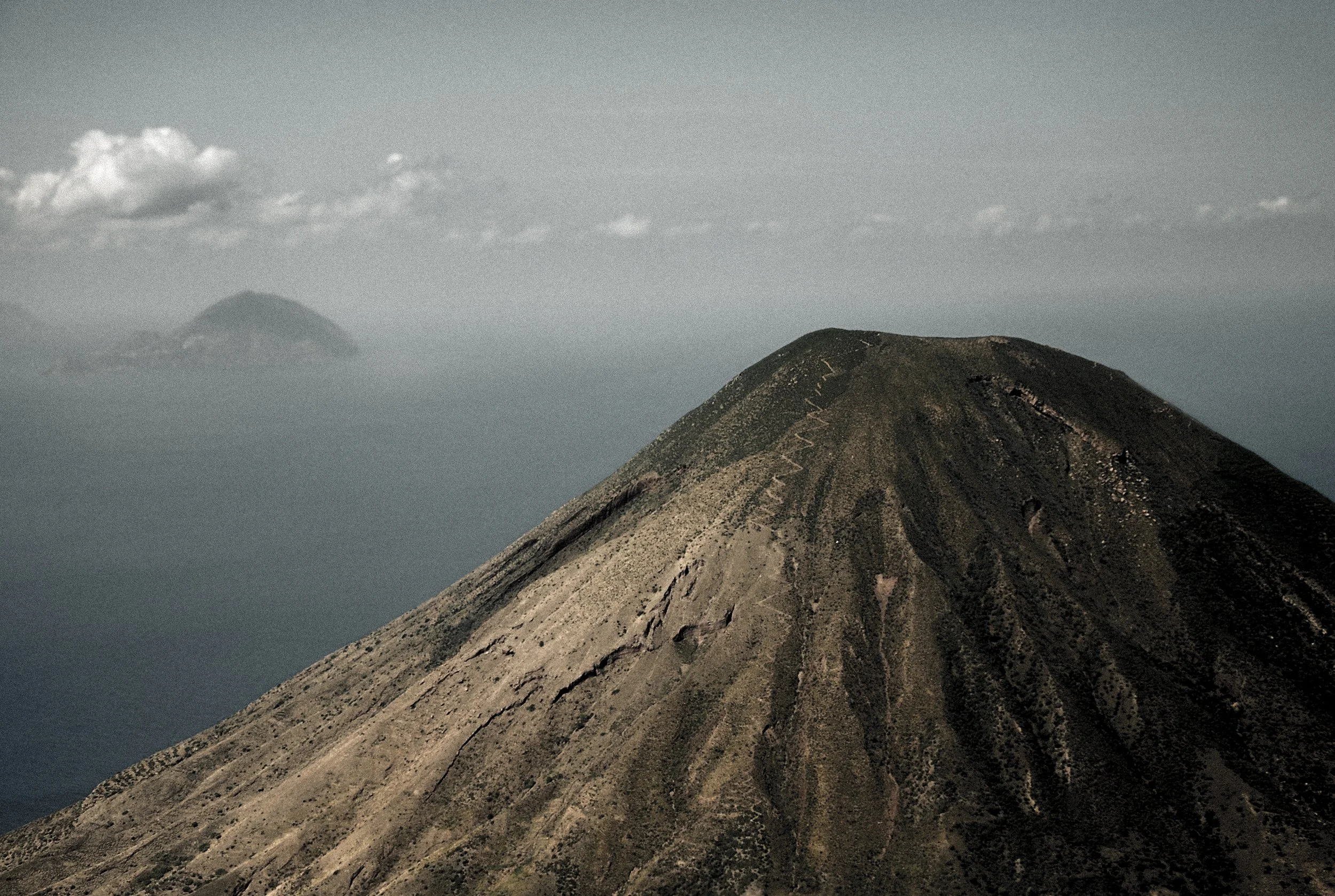Montagne volcanique avec un sommet arrondi, des traces de lave ou de cendres, et un ciel nuageux en arrière-plan.