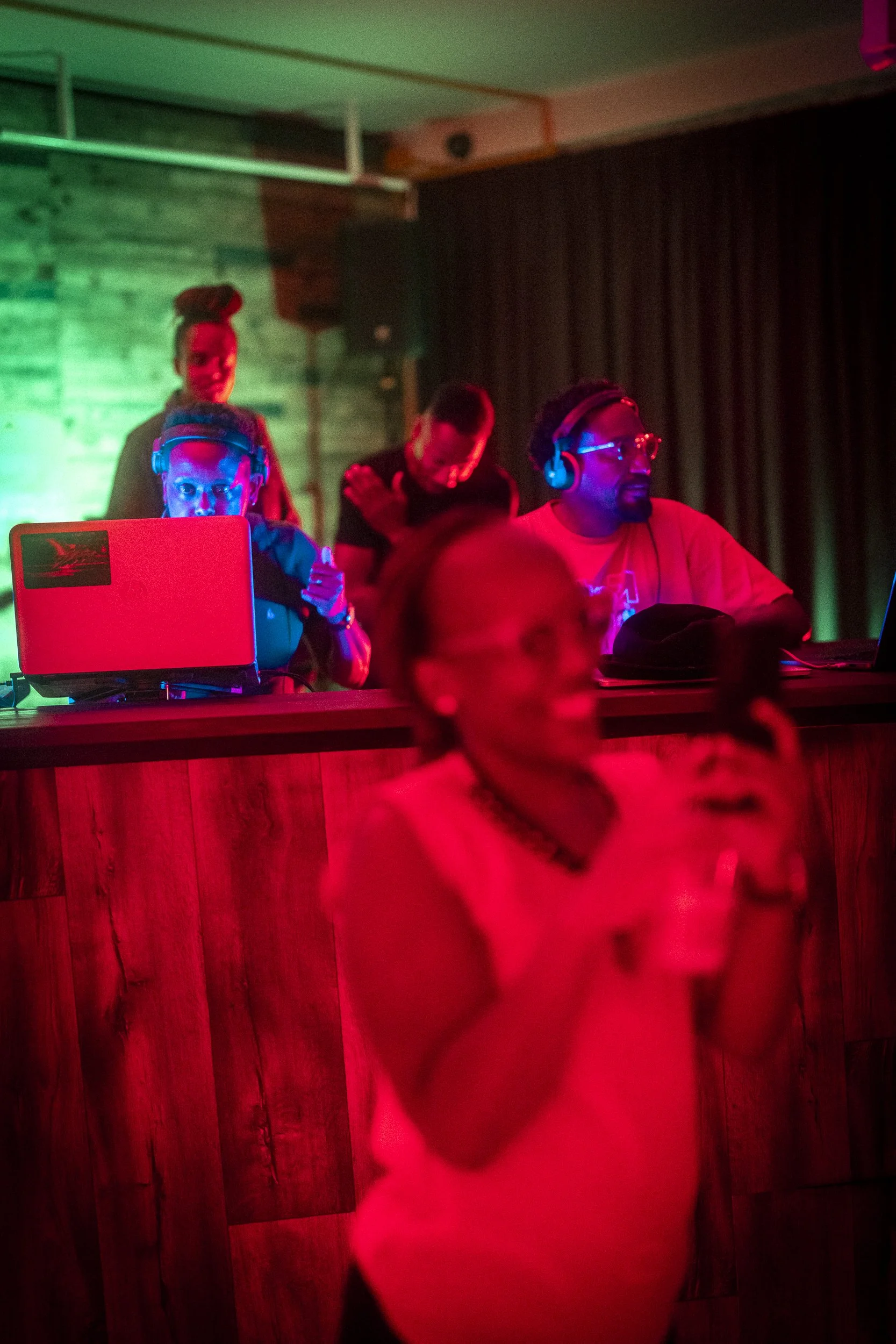 Djs and people dancing in a nightclub with colorful lighting.