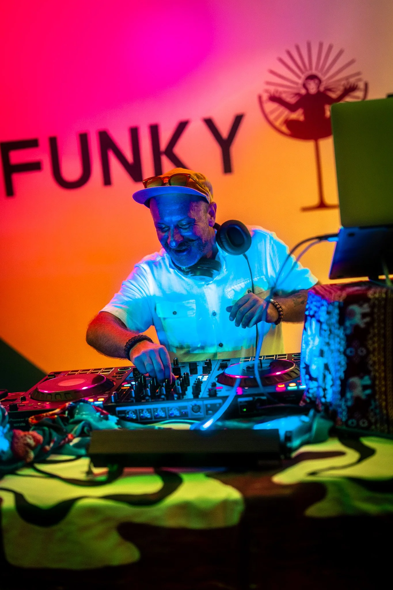 DJ at a colorful nightclub mixing music with a vibrant pink, orange, and yellow background that says 'FUNKY' and features a silhouette of a dancer.