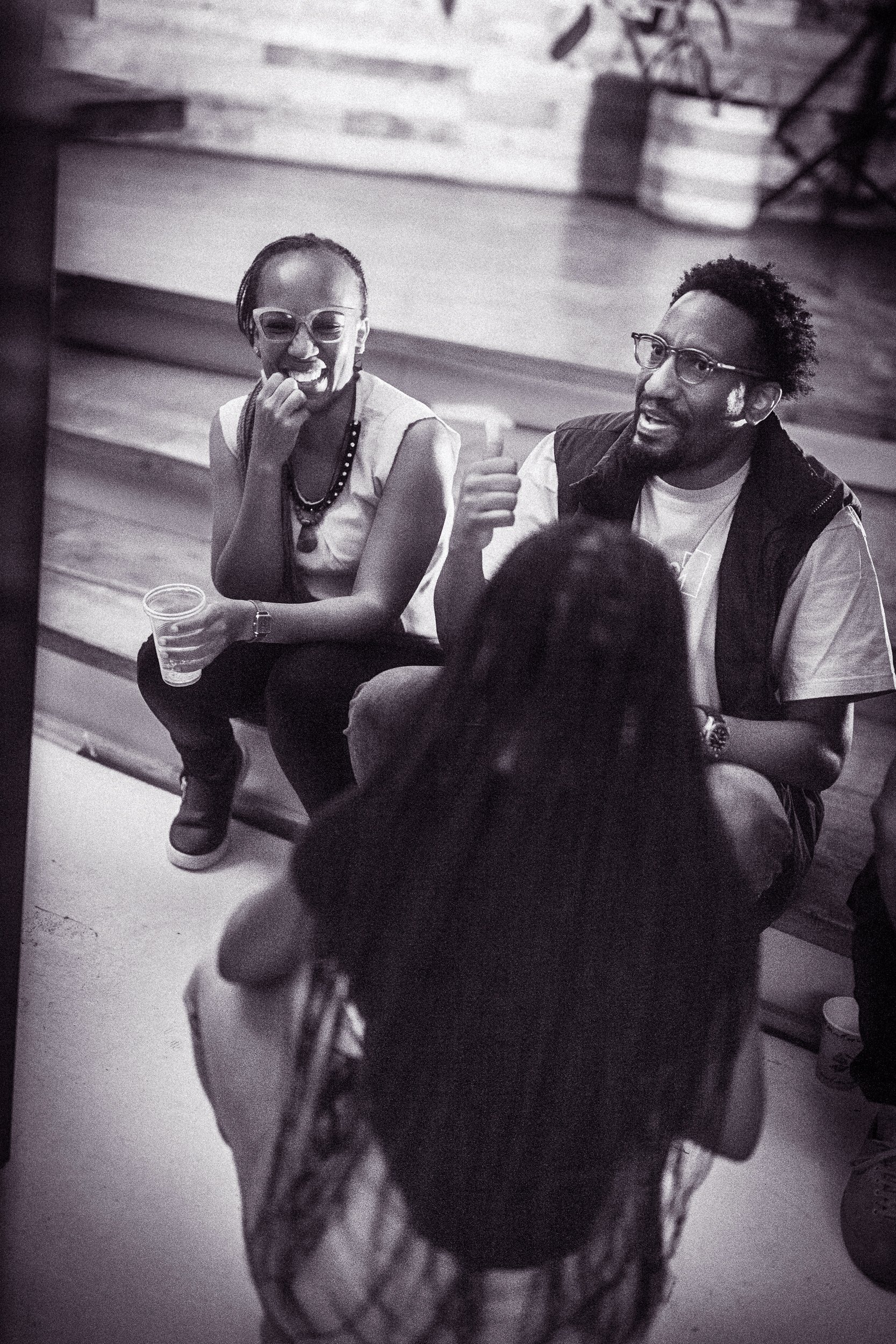 Three people engaged in conversation; two are sitting on stairs, one is standing in front of them.