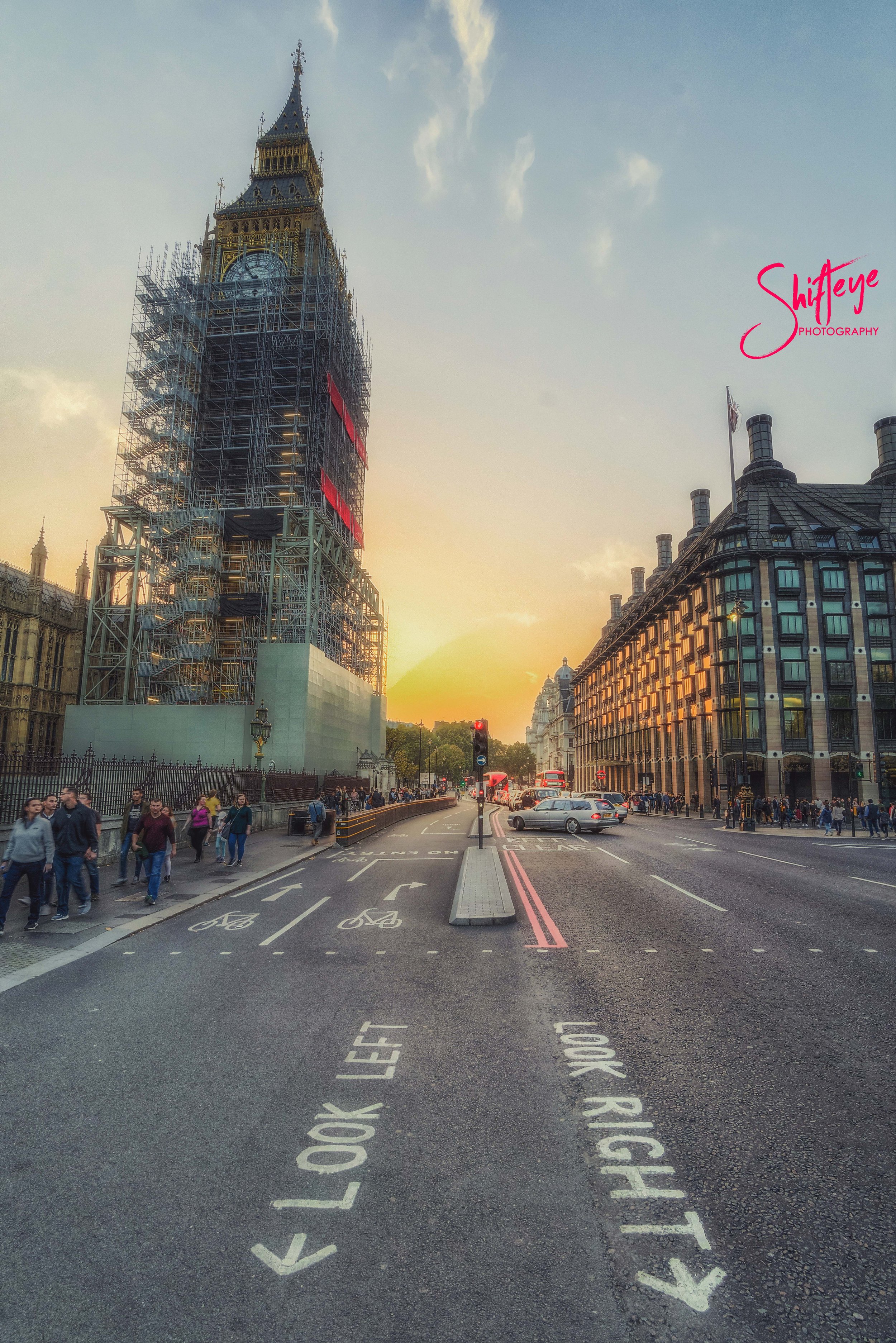 Big Ben under scaffolding in London with pedestrians and traffic, during sunset.