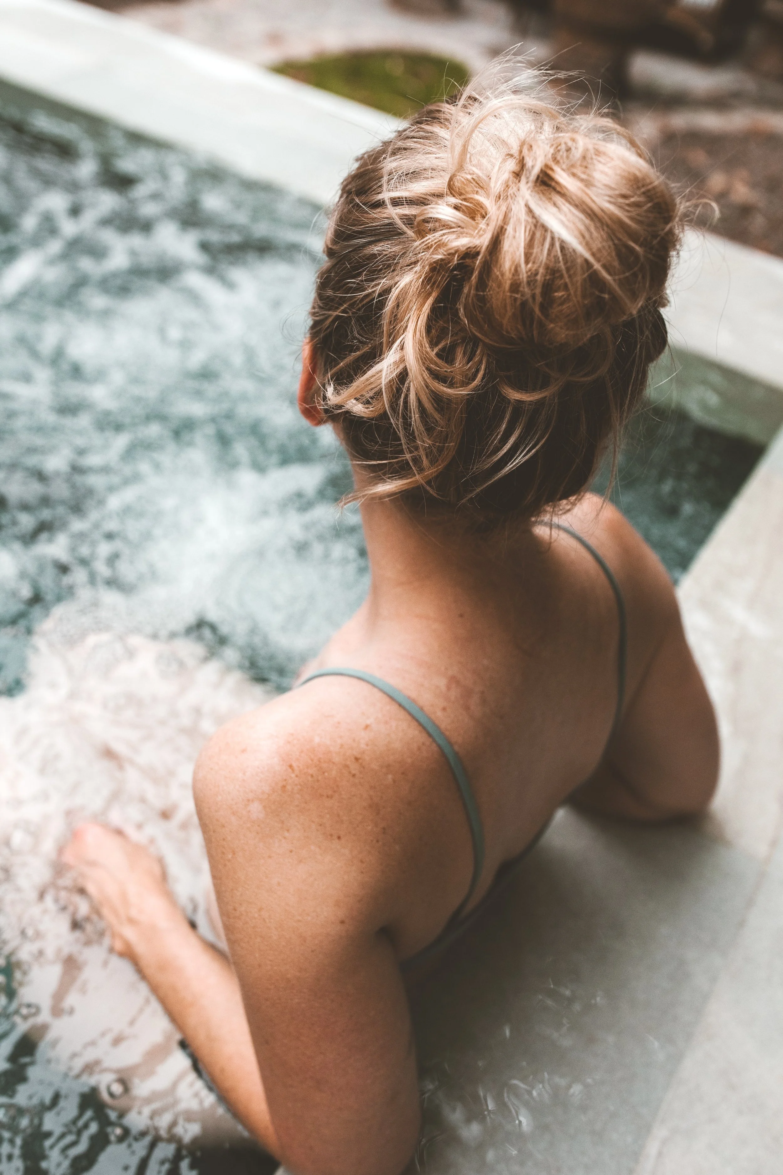 Woman with a curly updo hairstyle soaking in an outdoor hot tub or pool.