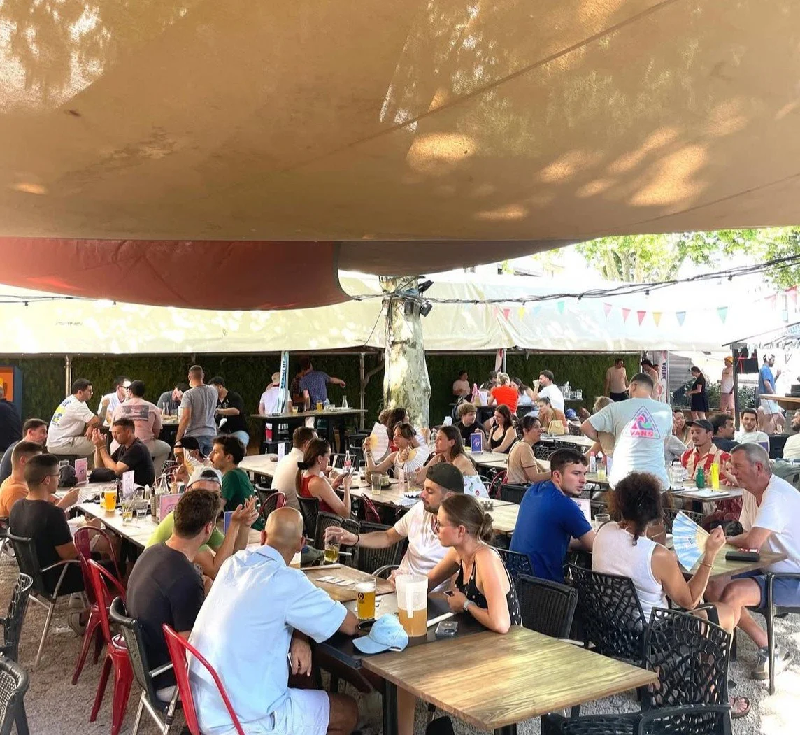 La terrasse ombragée du restaurant la Guinguette du 7 en plein air avec de nombreuses personnes assises à des tables;