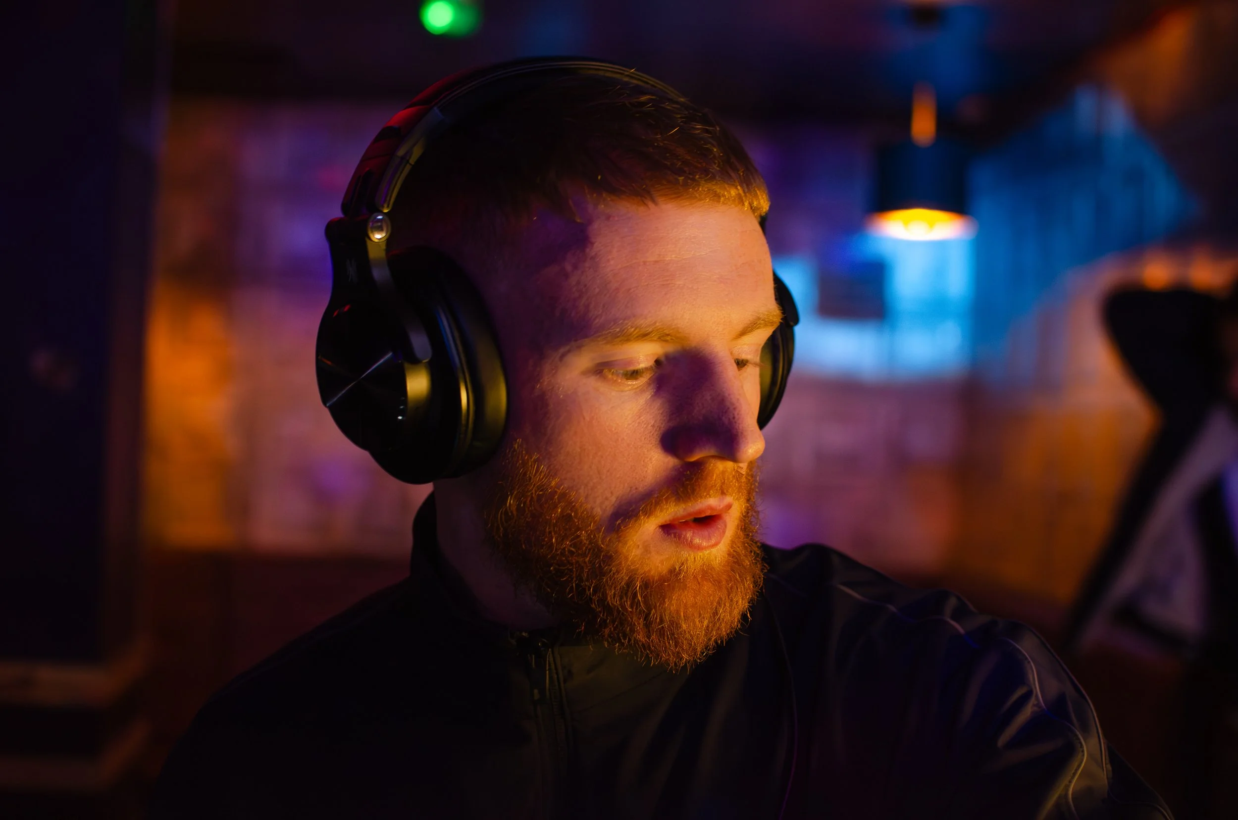 Man wearing headphones in a dimly lit room with colored lighting.