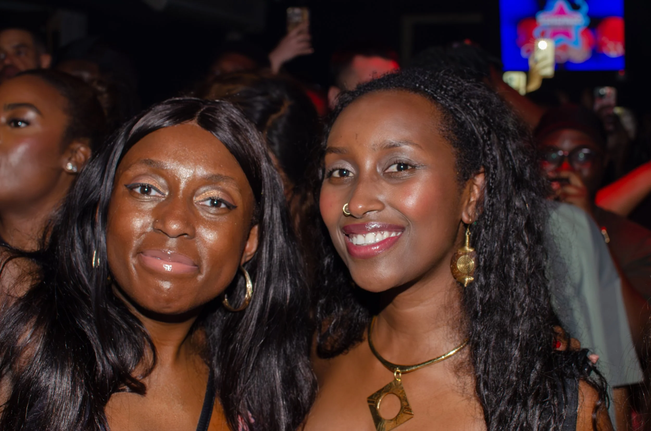 Two women smiling at an event, surrounded by a crowd.
