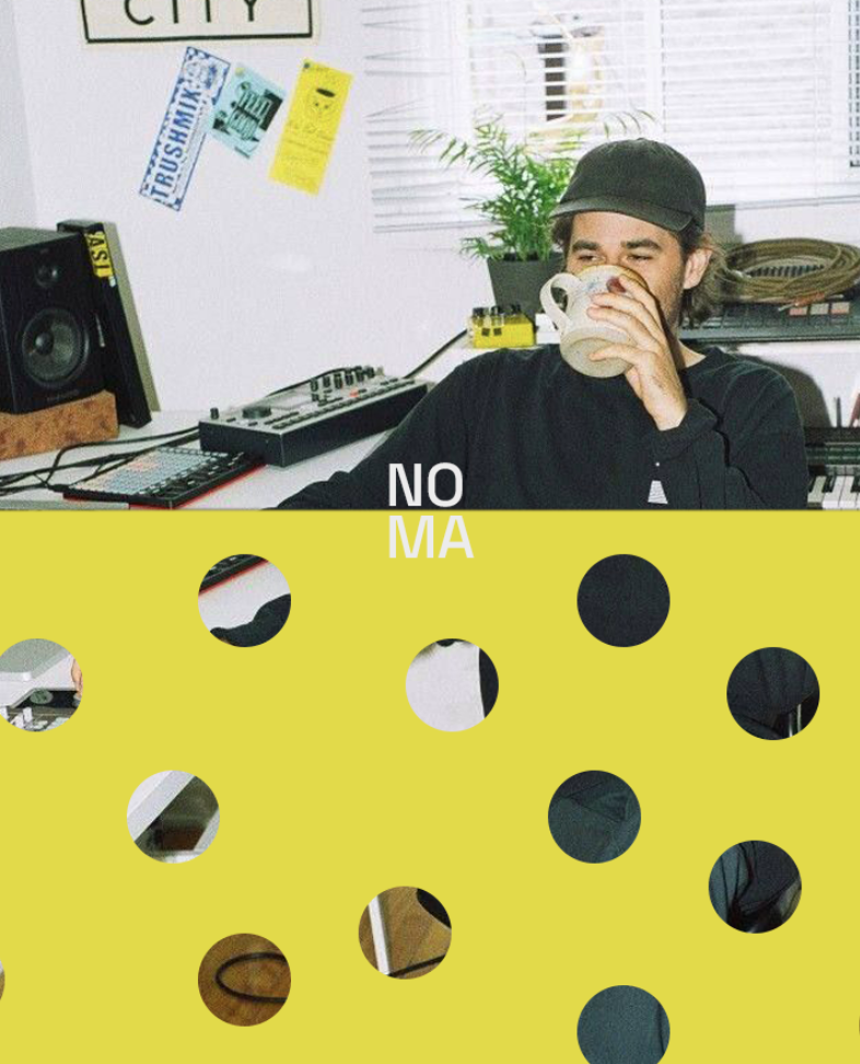 A man wearing a black cap drinks from a mug while sitting in a home studio or office, with musical equipment and a plant in the background.