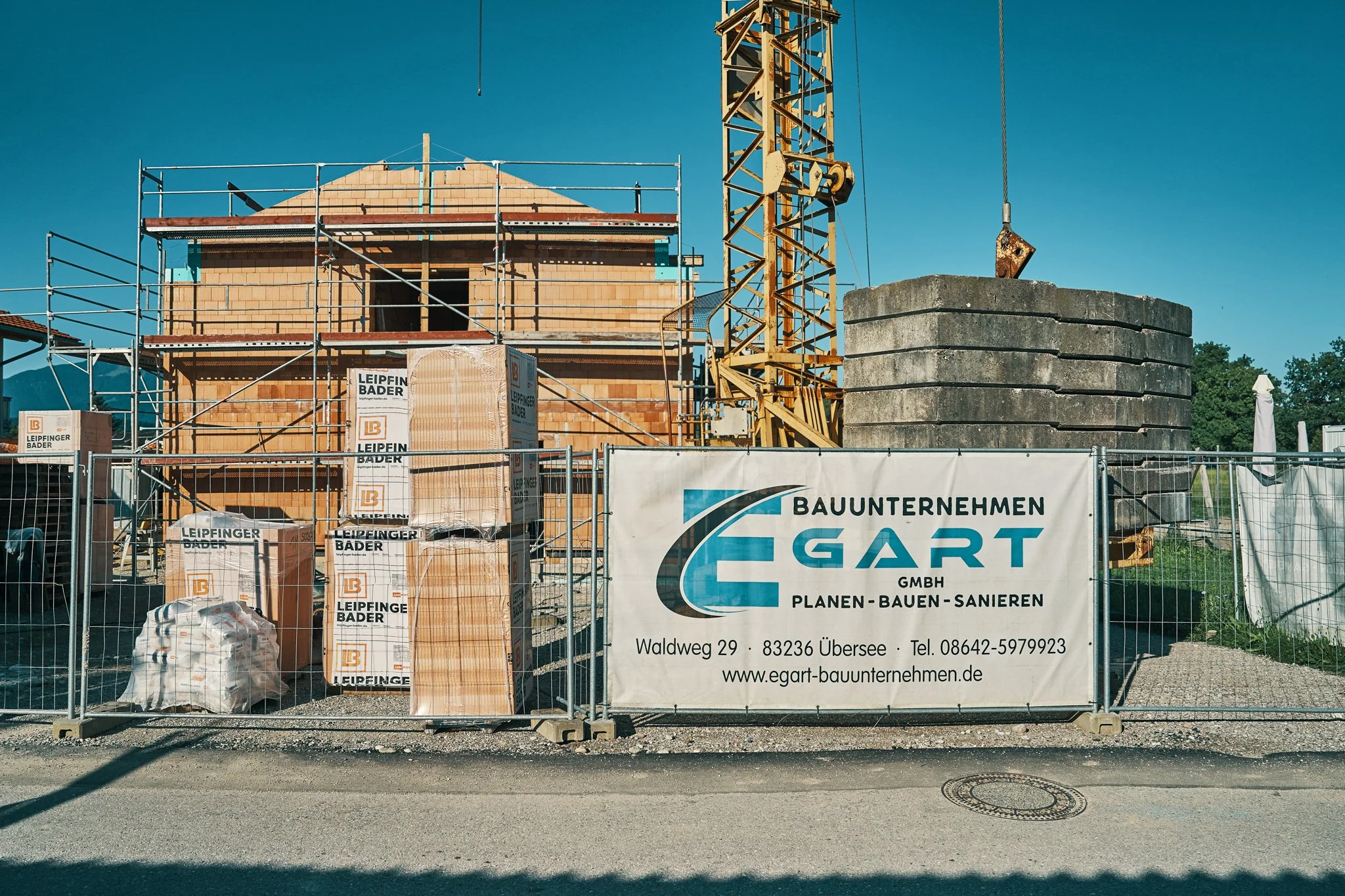 EGART GmbH Baustelle mit Baugerüst, Zementsilos und Firmenbanner am Standort Waldweg 29 in Übersee (Chiemgau), Deutschland.