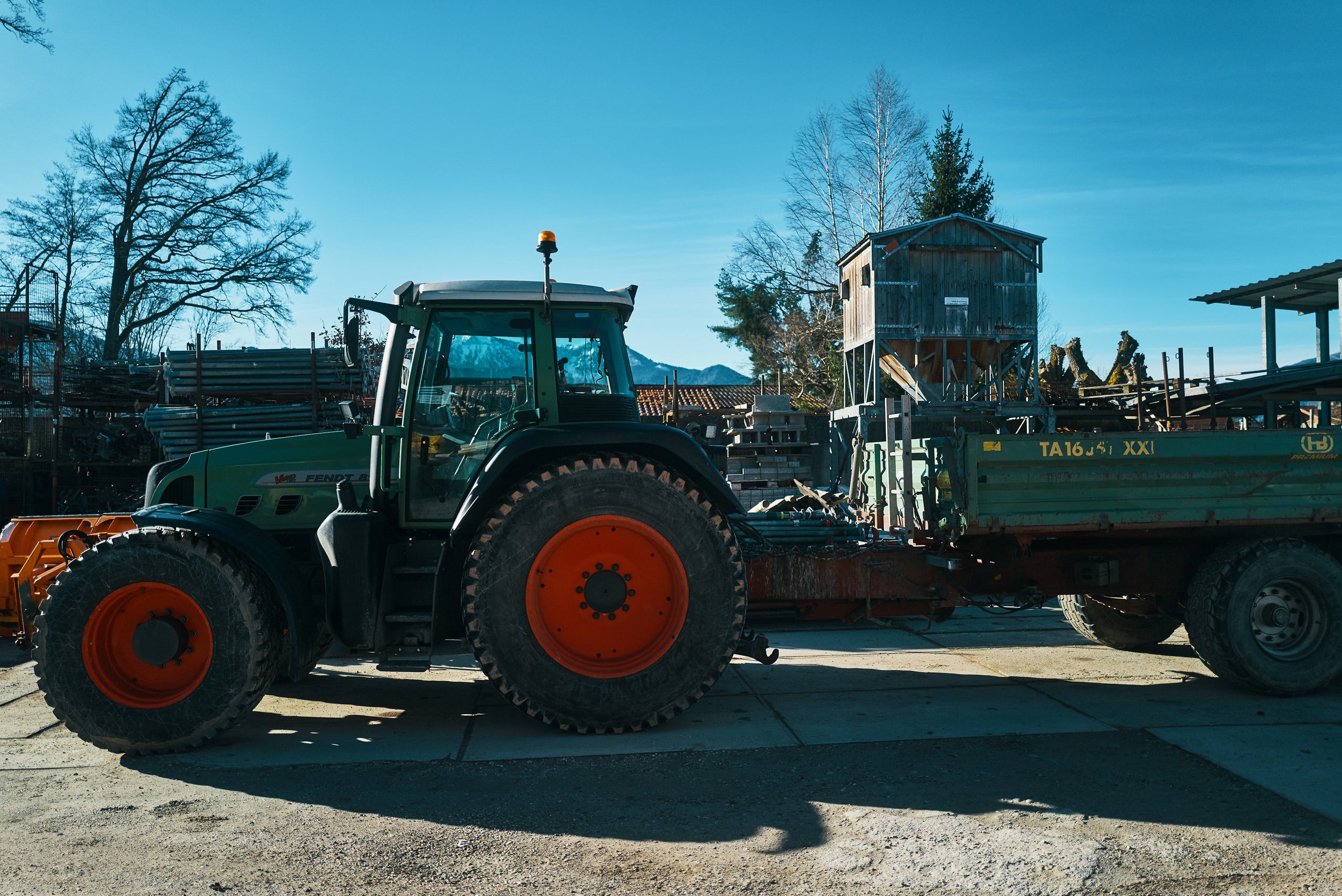 EGART Traktor auf Bauernhof mit landwirtschaftlichem Gerät im Hintergrund bei Tageslicht.