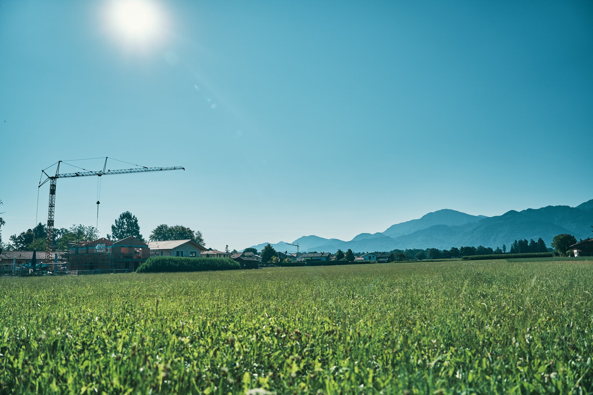 EGART Baustelle im Grünen: Blick auf ein Feld mit Neubauten, Baukran und Bergen im Hintergrund unter blauem Himmel.