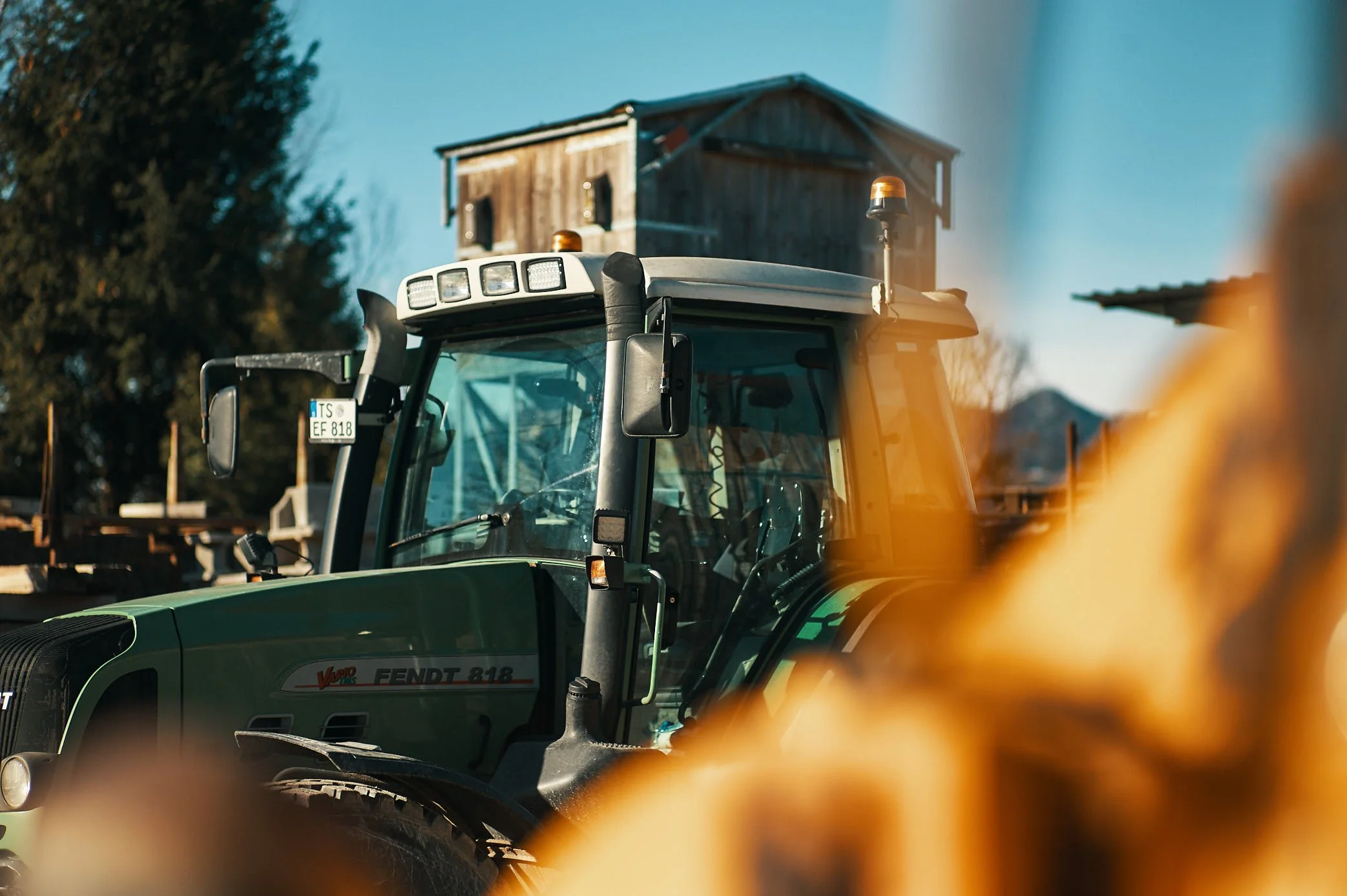 EGART Traktor auf Feld vor altem Holzhaus, landwirtschaftliche Szene bei Sonnenschein.