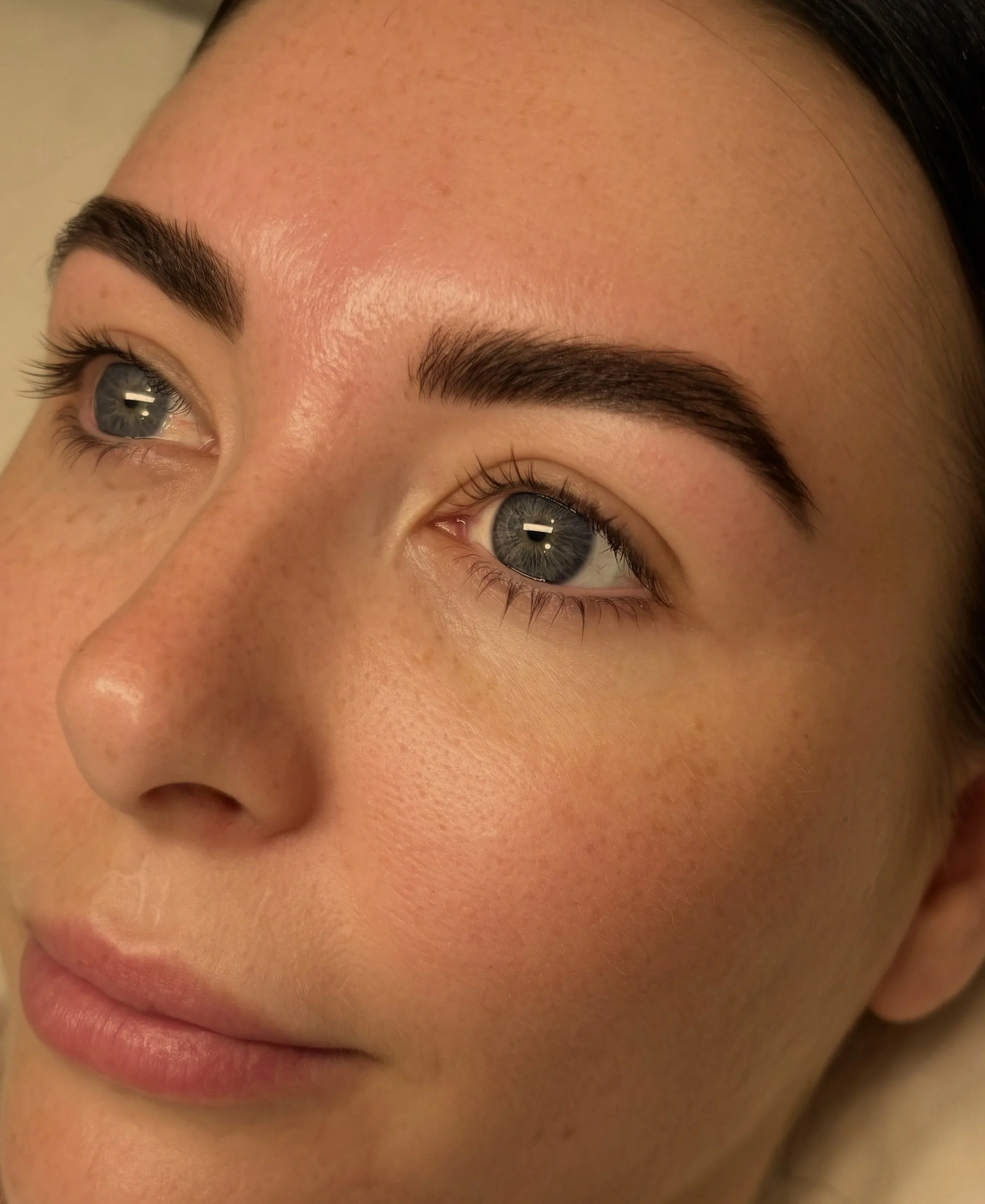 Close-up of a woman's face showing her blue eyes, dark eyebrows, and clear skin.