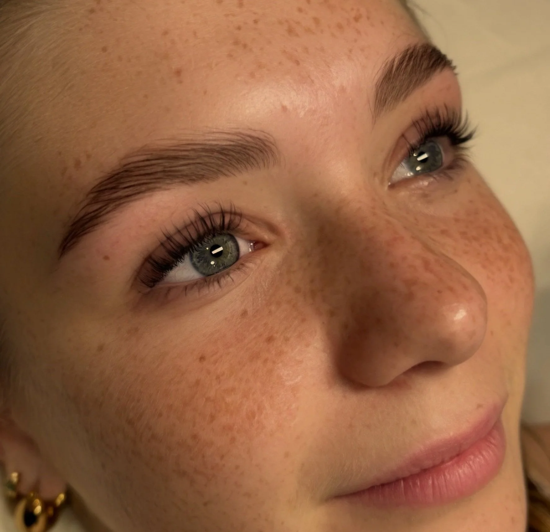 Close-up of a young woman's face, showing her blue eyes, freckles, and lightly colored lips.
