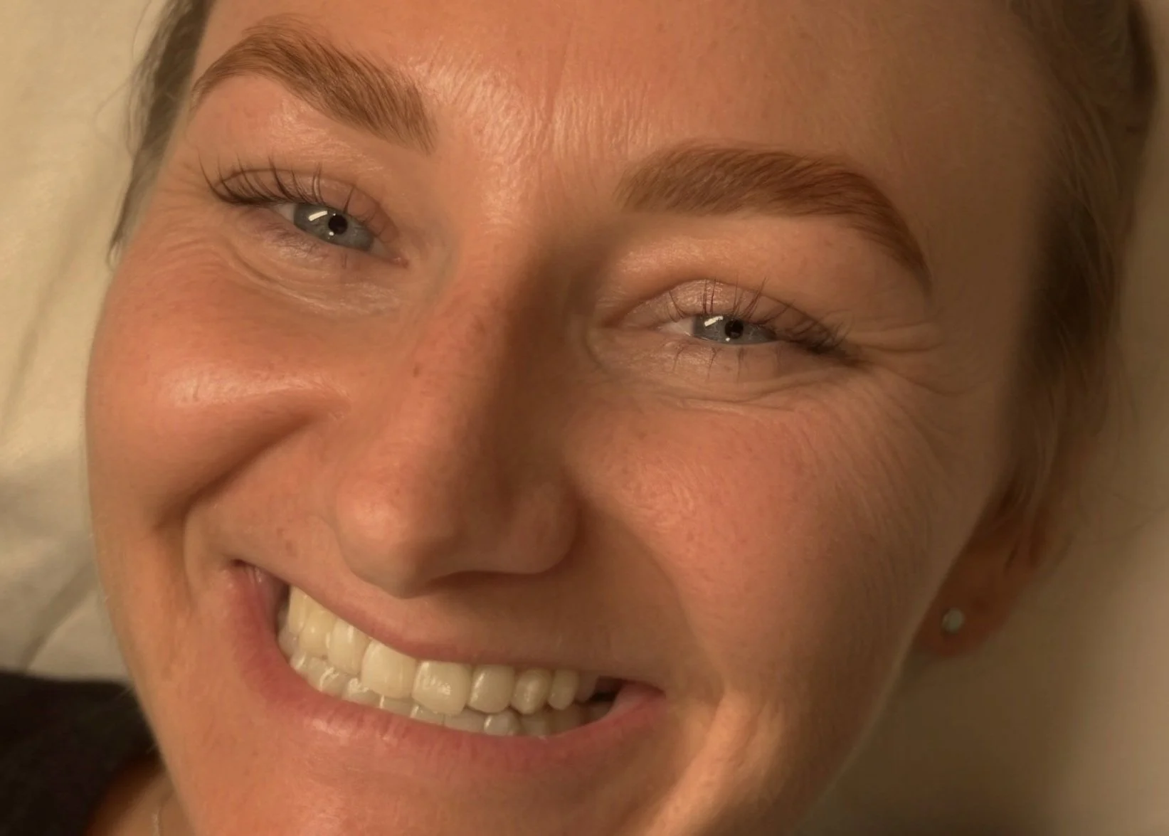 Close-up of a smiling woman with blonde hair, blue eyes, and light skin.