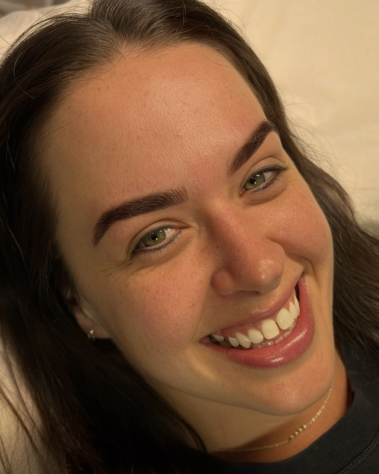 Close-up of a woman's smiling face with dark hair, green eyes, and well-groomed eyebrows.