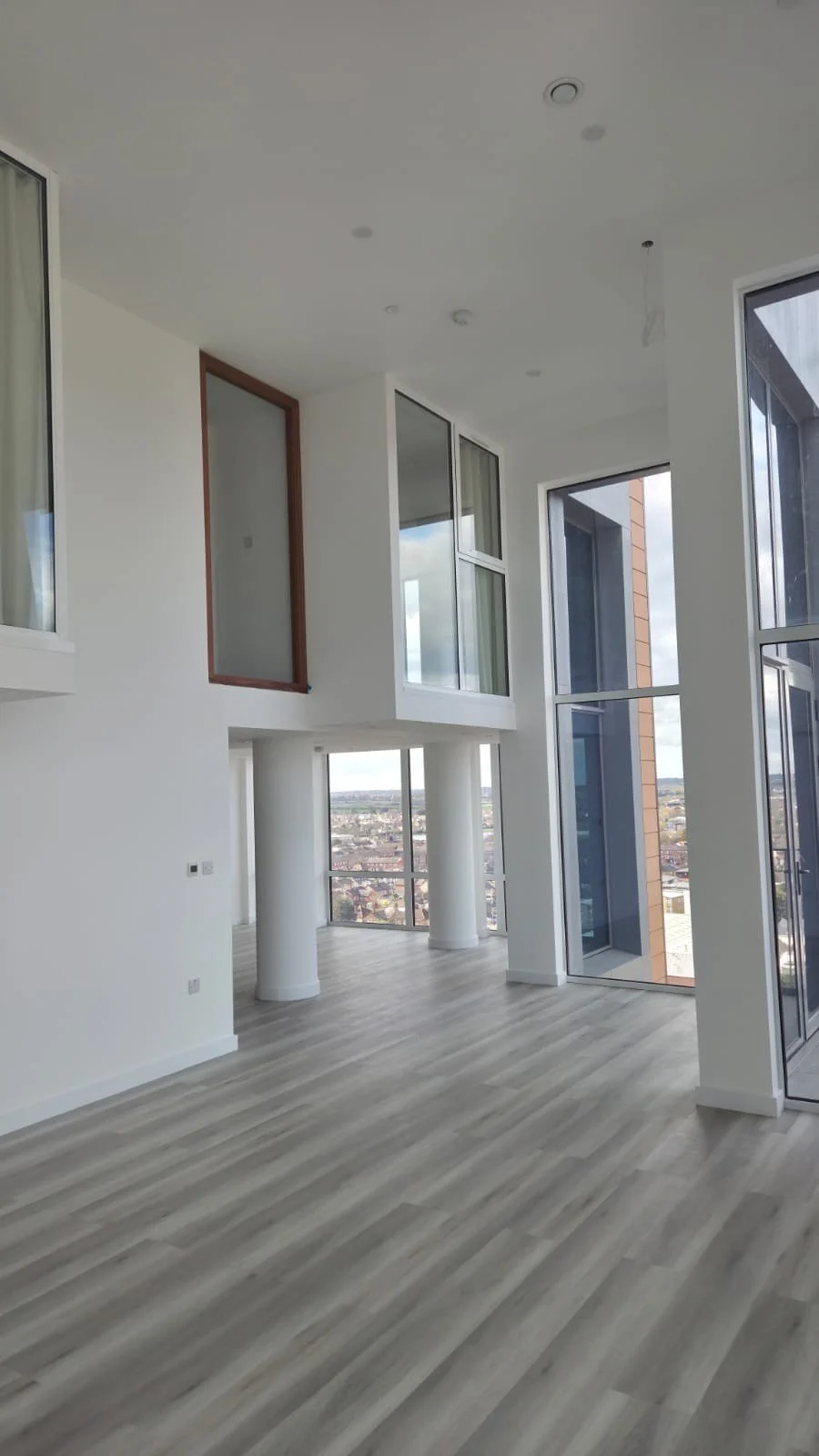 Interior of a modern, empty apartment with large windows and light wood flooring.