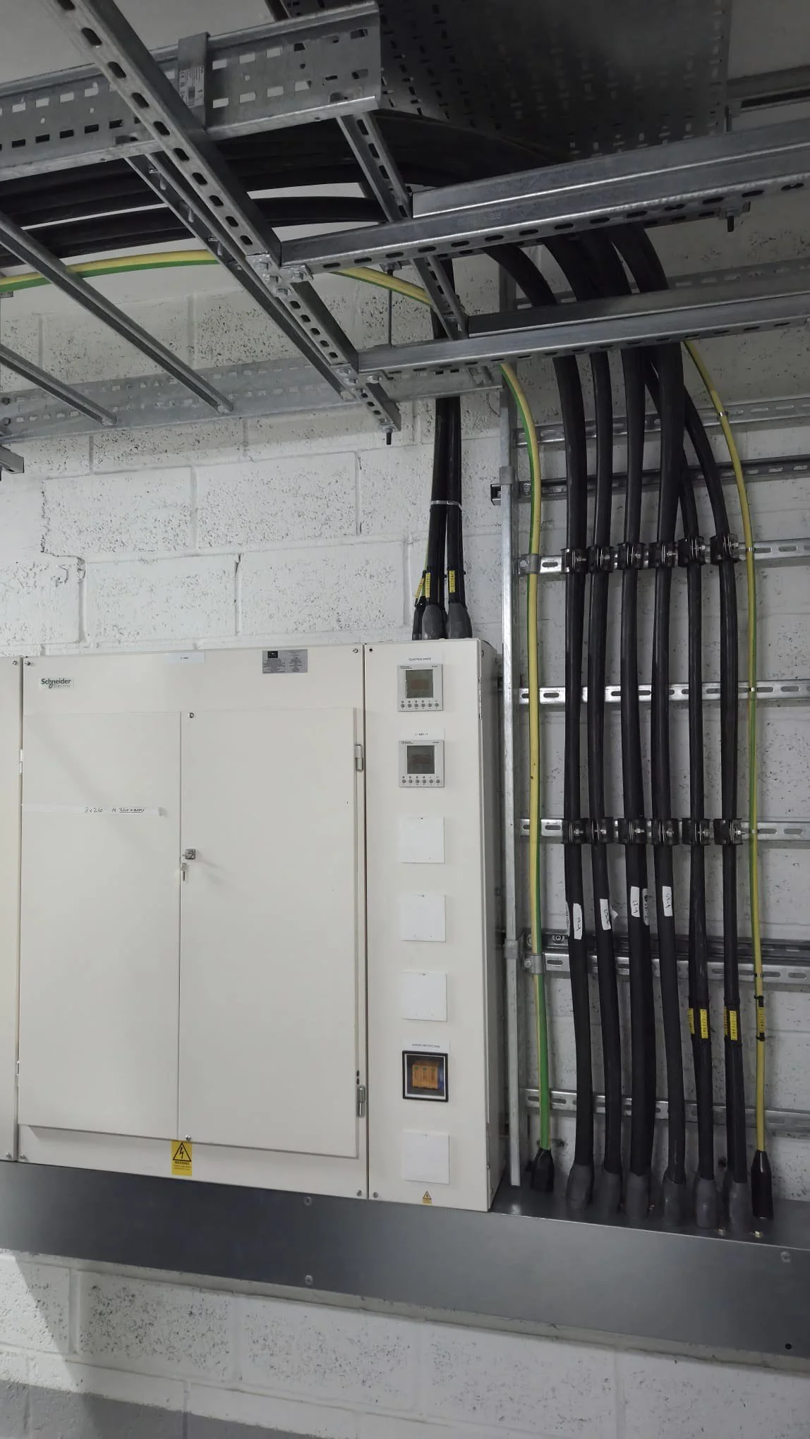 Electrical panel with black and yellow cables organized in conduit, mounted on a concrete wall.
