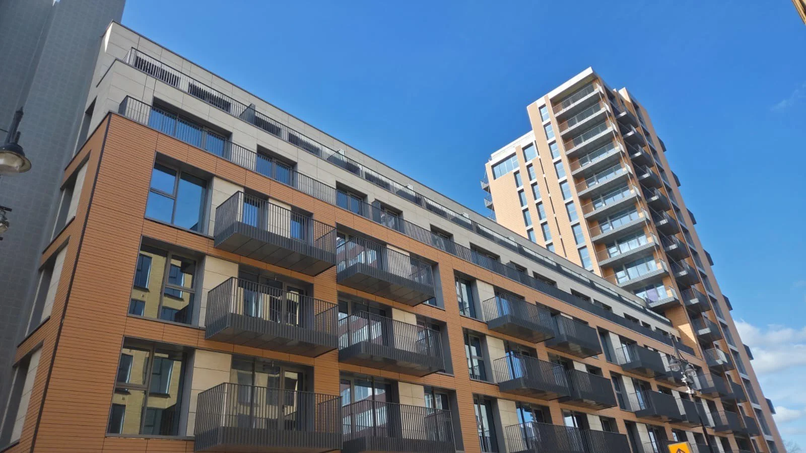 Modern multi-story apartment building with balconies and large windows against a blue sky.