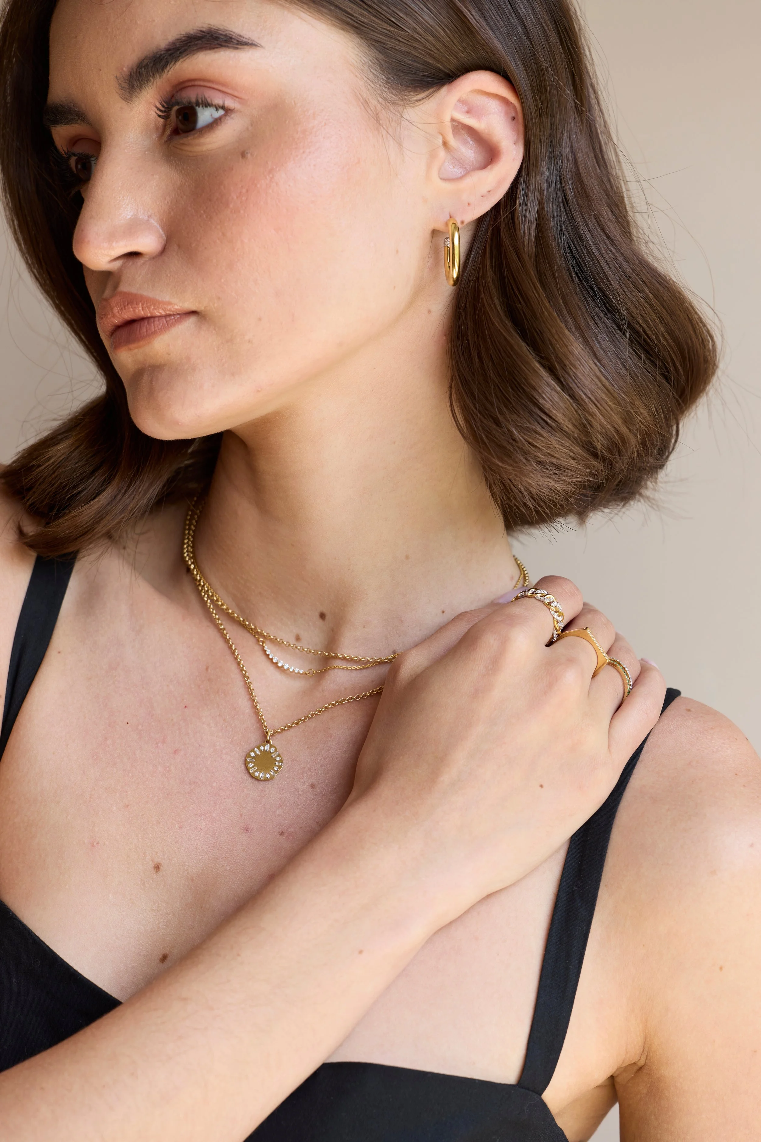 Model wearing 14k gold necklaces, 14k gold hoop earrings, and 14k rings by Zikr Fine Jewelry