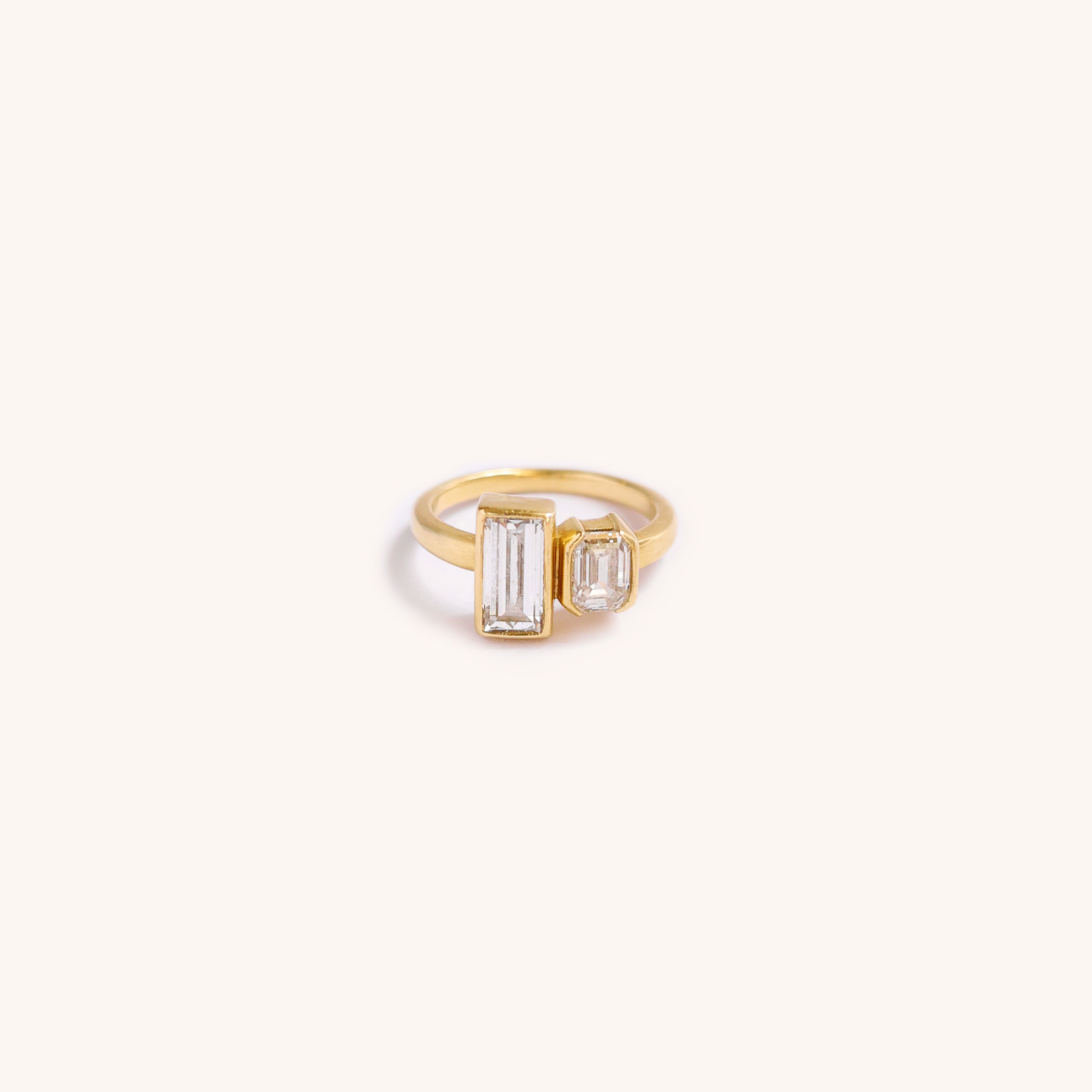 Gold ring with two clear rectangular and octagonal gemstones on a plain white background.