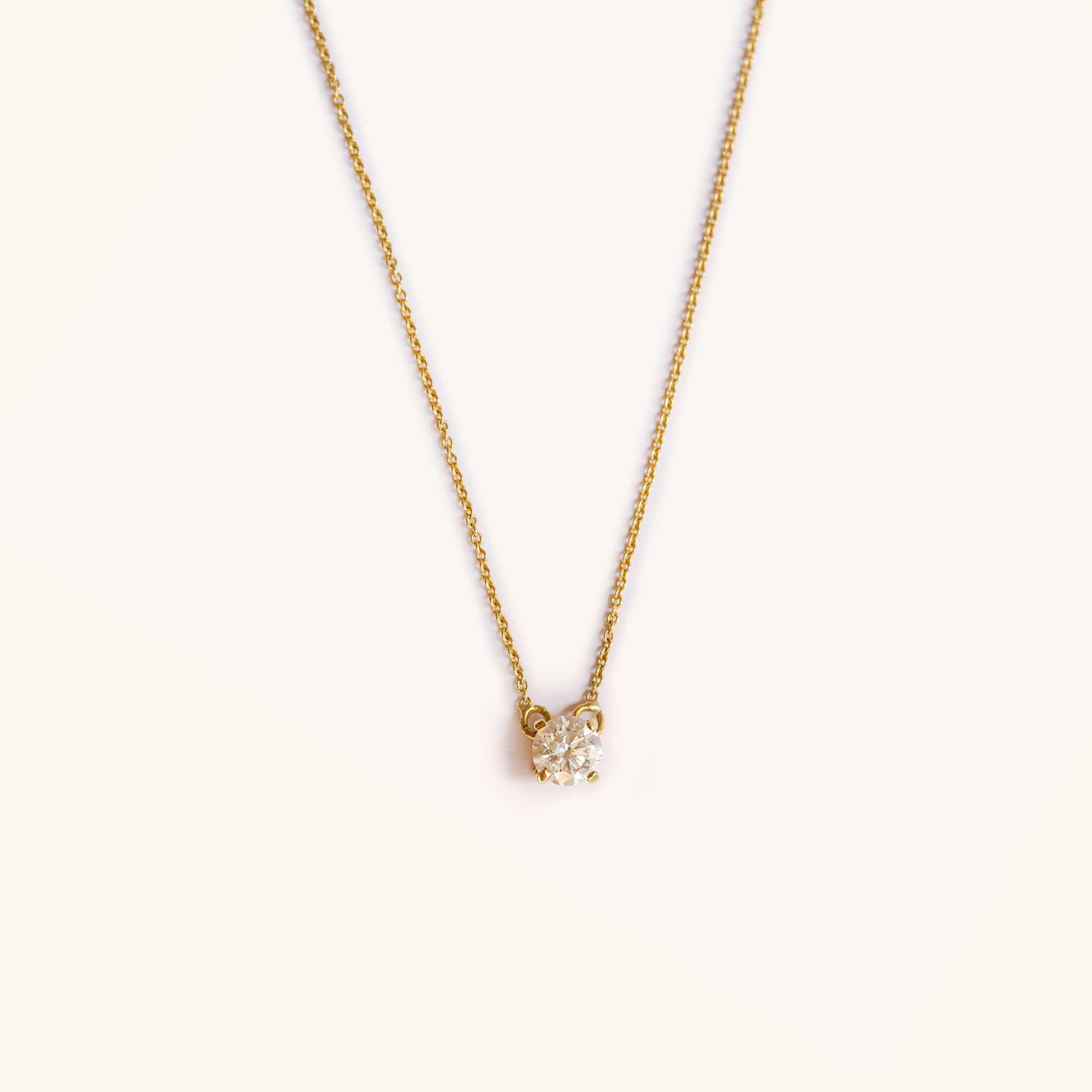 Gold necklace with a single round diamond pendant against a white background.