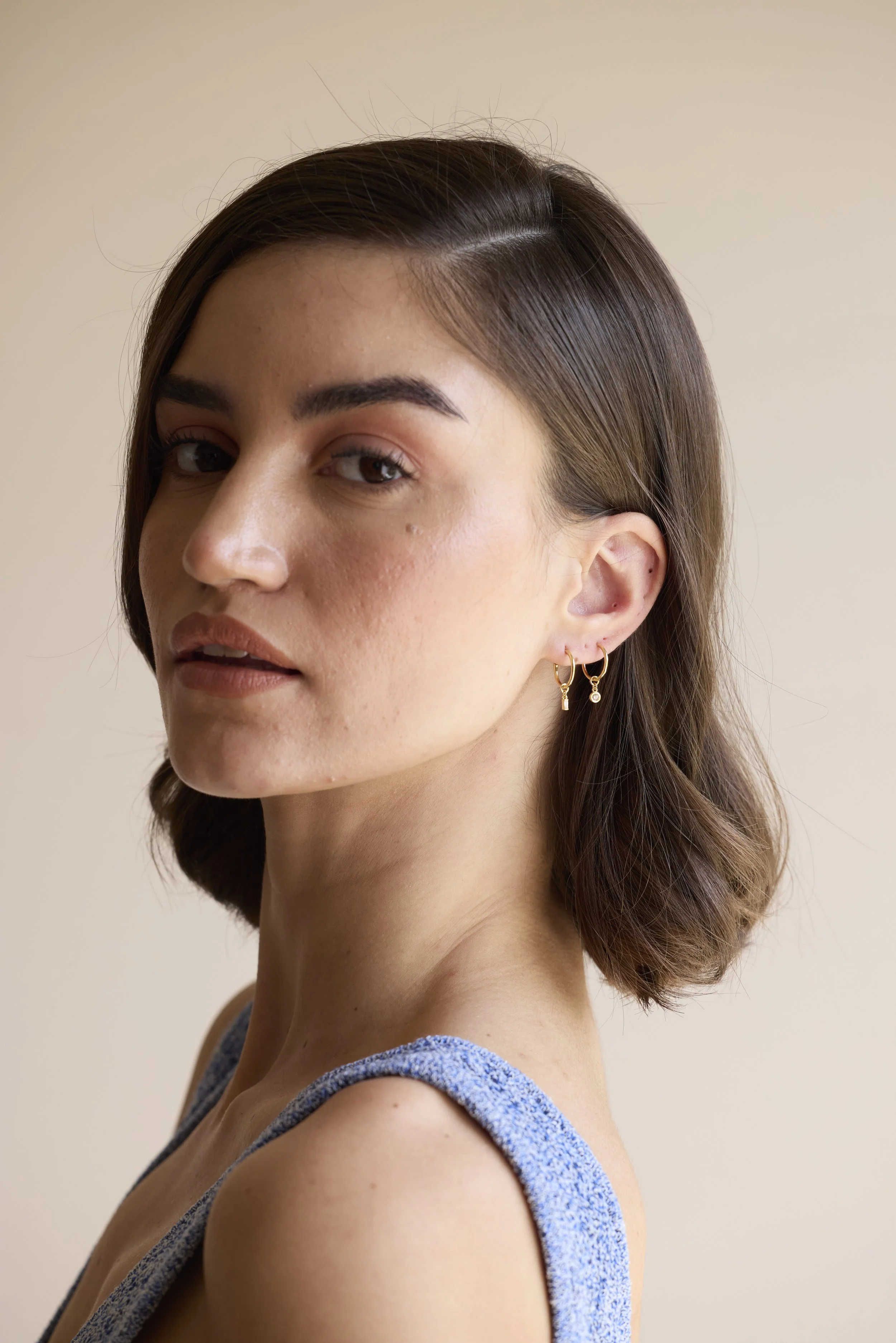 14K gold diamond hoop earrings with mismatched charms, one round-cut diamond and one baguette diamond, handmade luxury jewelry by Zikr Fine Jewelry.