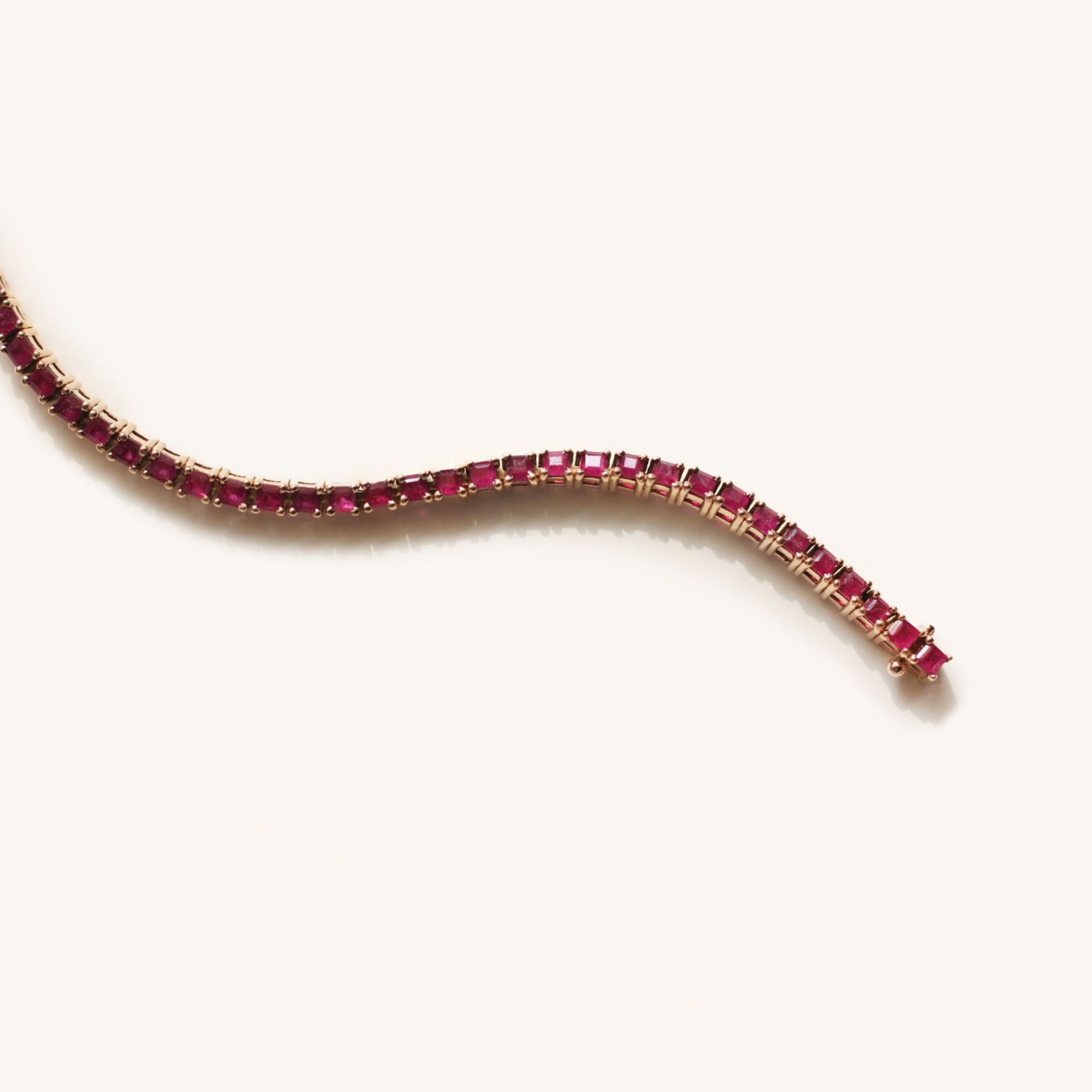 A gold necklace with rectangular pink gemstones, arranged in a row, shown against a plain off-white background.