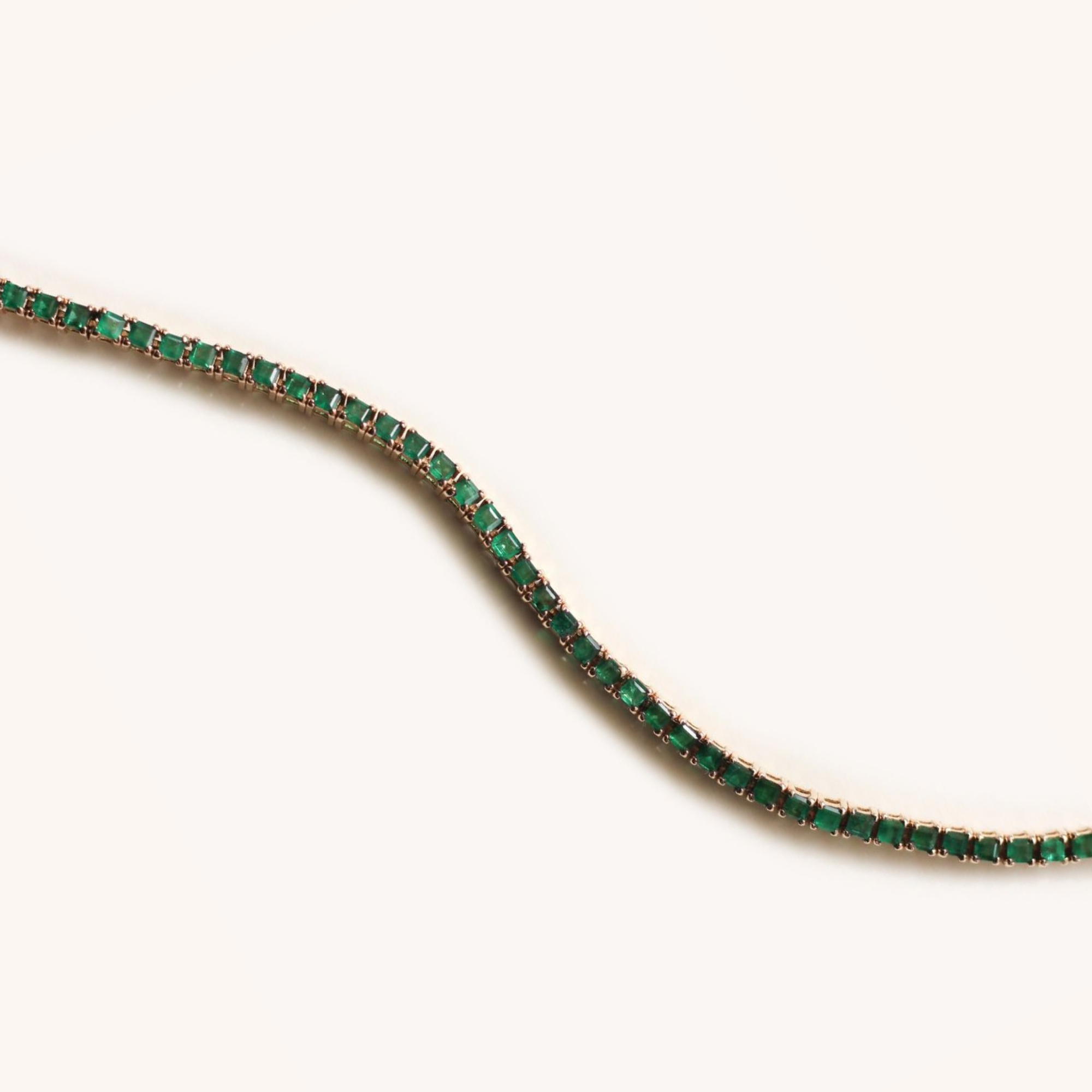 A curved row of emerald and diamond jewelry on a white background.