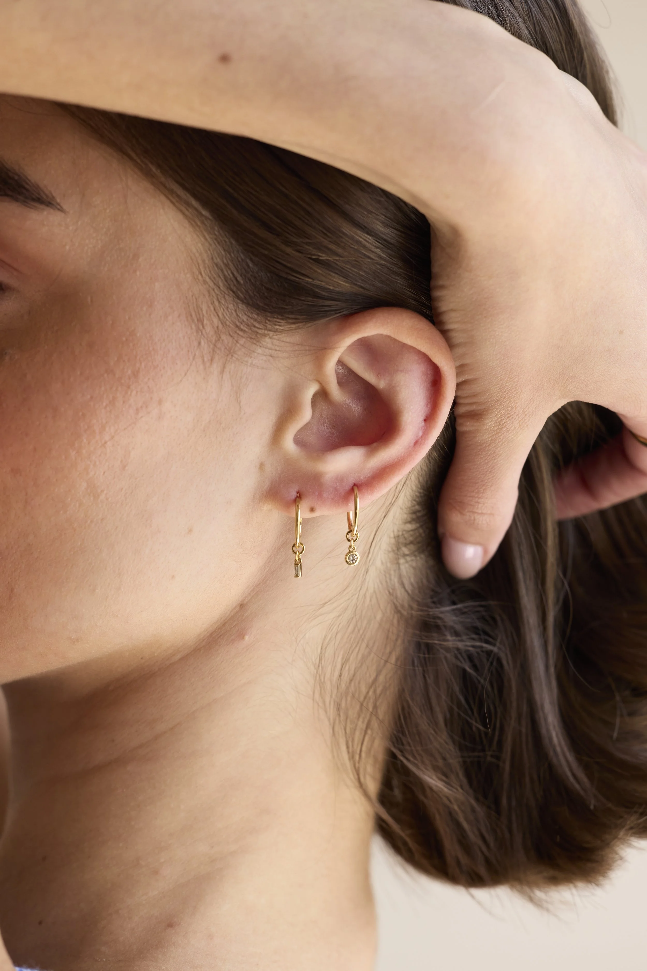 14K gold diamond hoop earrings with mismatched charms, one round-cut diamond and one baguette diamond, handmade luxury jewelry by Zikr Fine Jewelry.