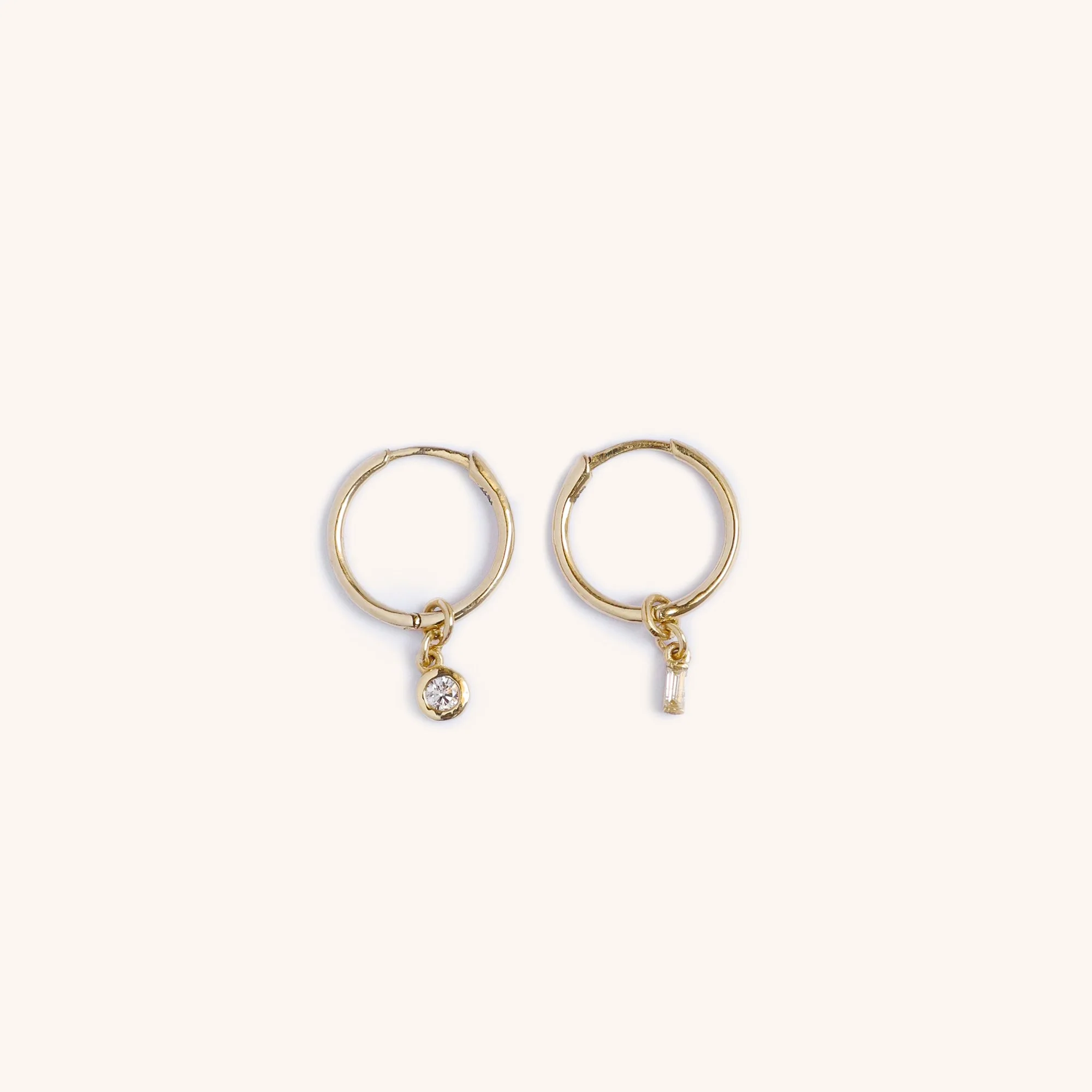 14K gold diamond hoop earrings with mismatched charms, one round-cut diamond and one baguette diamond, handmade luxury jewelry by Zikr Fine Jewelry.