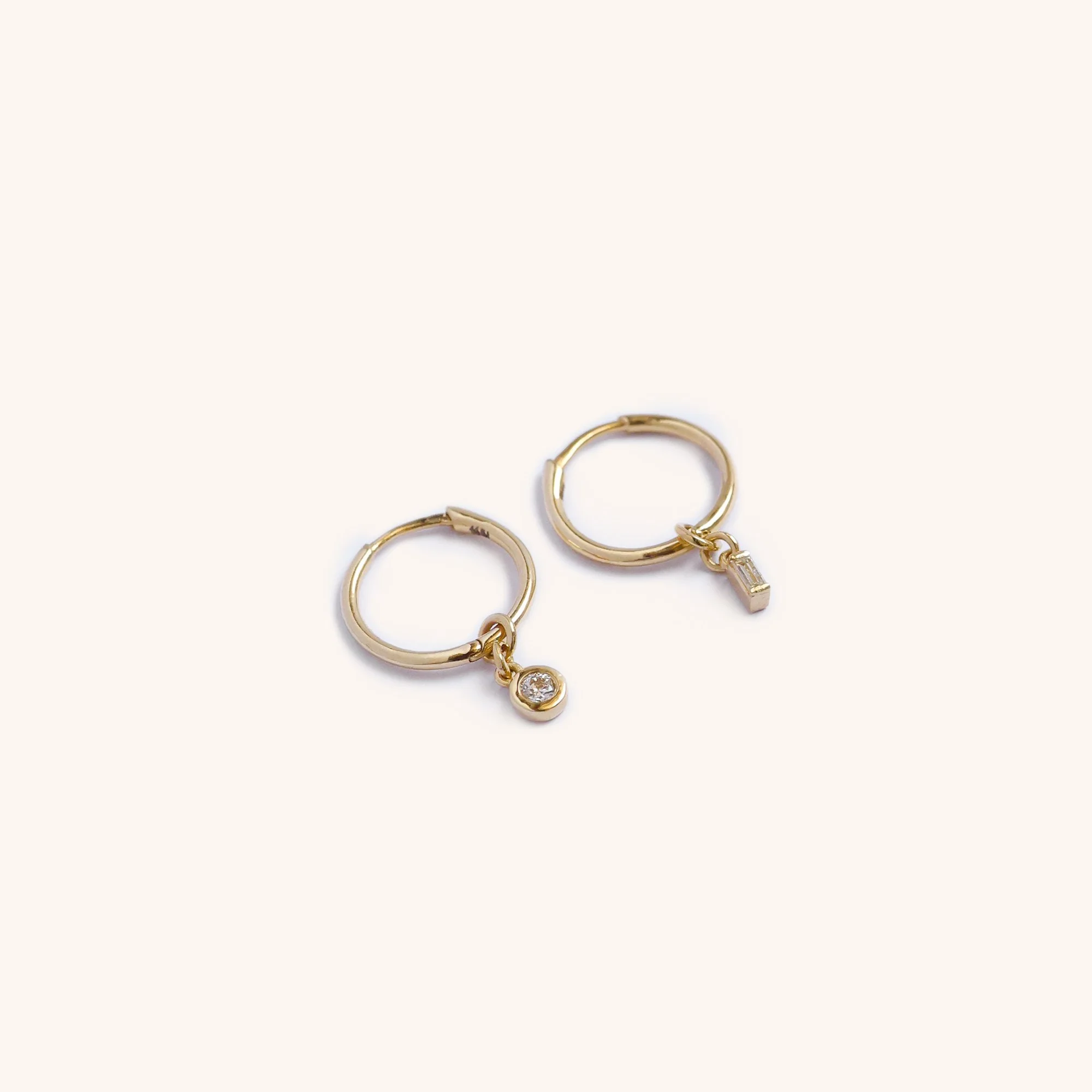 14K gold diamond hoop earrings with mismatched charms, one round-cut diamond and one baguette diamond, handmade luxury jewelry by Zikr Fine Jewelry.