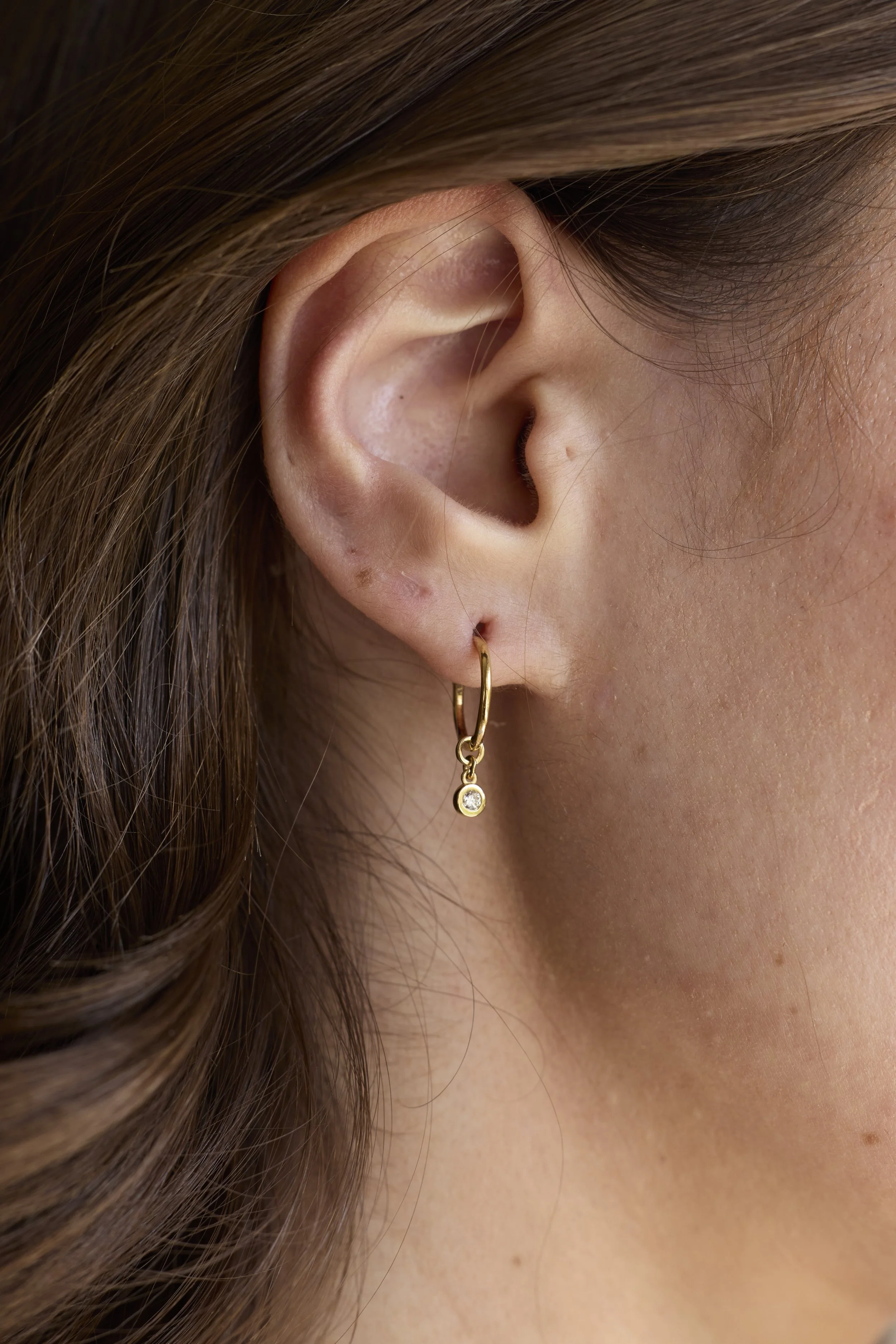 14K gold diamond hoop earrings with mismatched charms, one round-cut diamond and one baguette diamond, handmade luxury jewelry by Zikr Fine Jewelry.