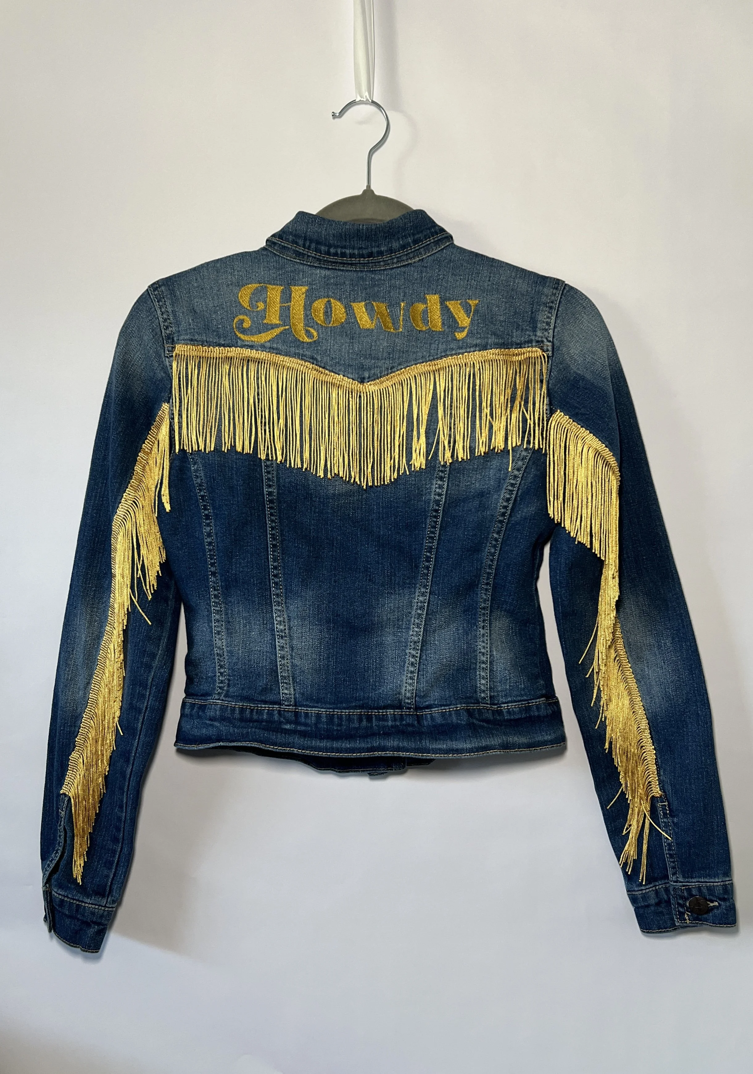 Denim jacket with yellow fringe and 'Howdy' text on back.
