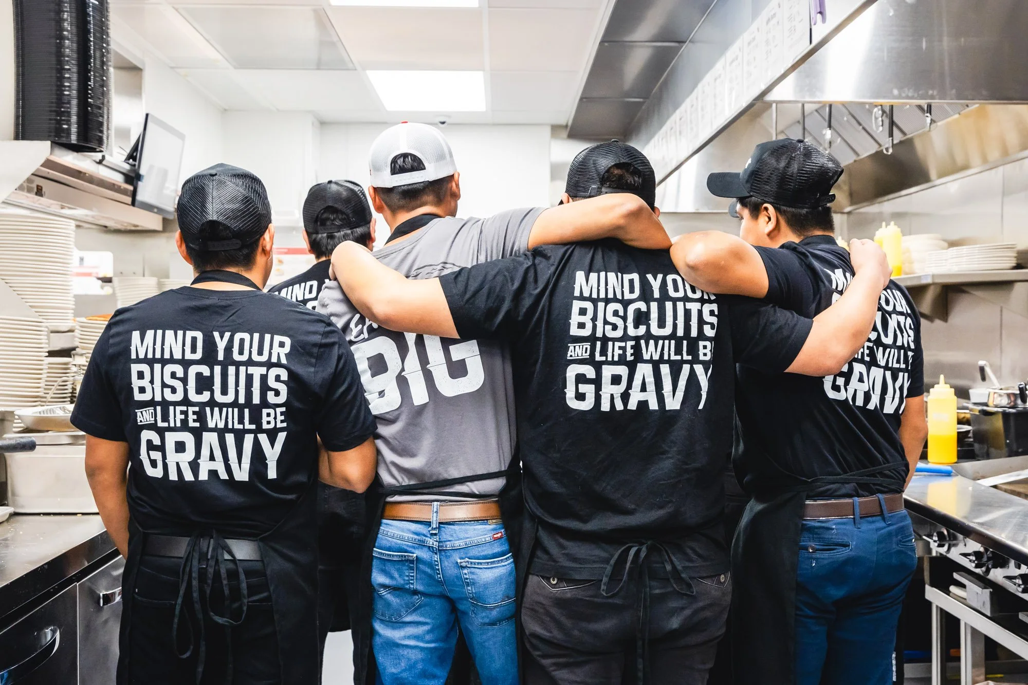 Big Biscuit kitchen staff standing together in the restaurant kitchen wearing branded shirts that read “Mind Your Biscuits and Life Will Be Gravy.”