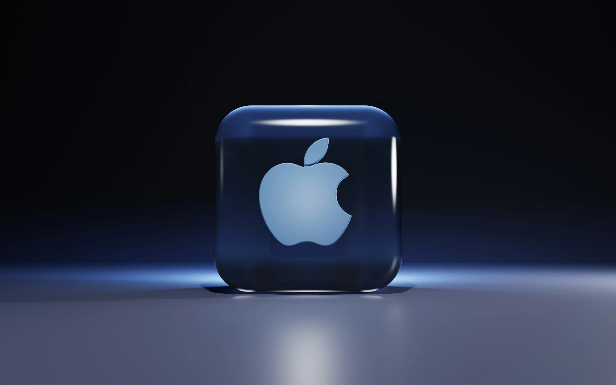 Close-up of a transparent glass cube with a white Apple logo illuminated inside, set against a dark background with soft lighting.