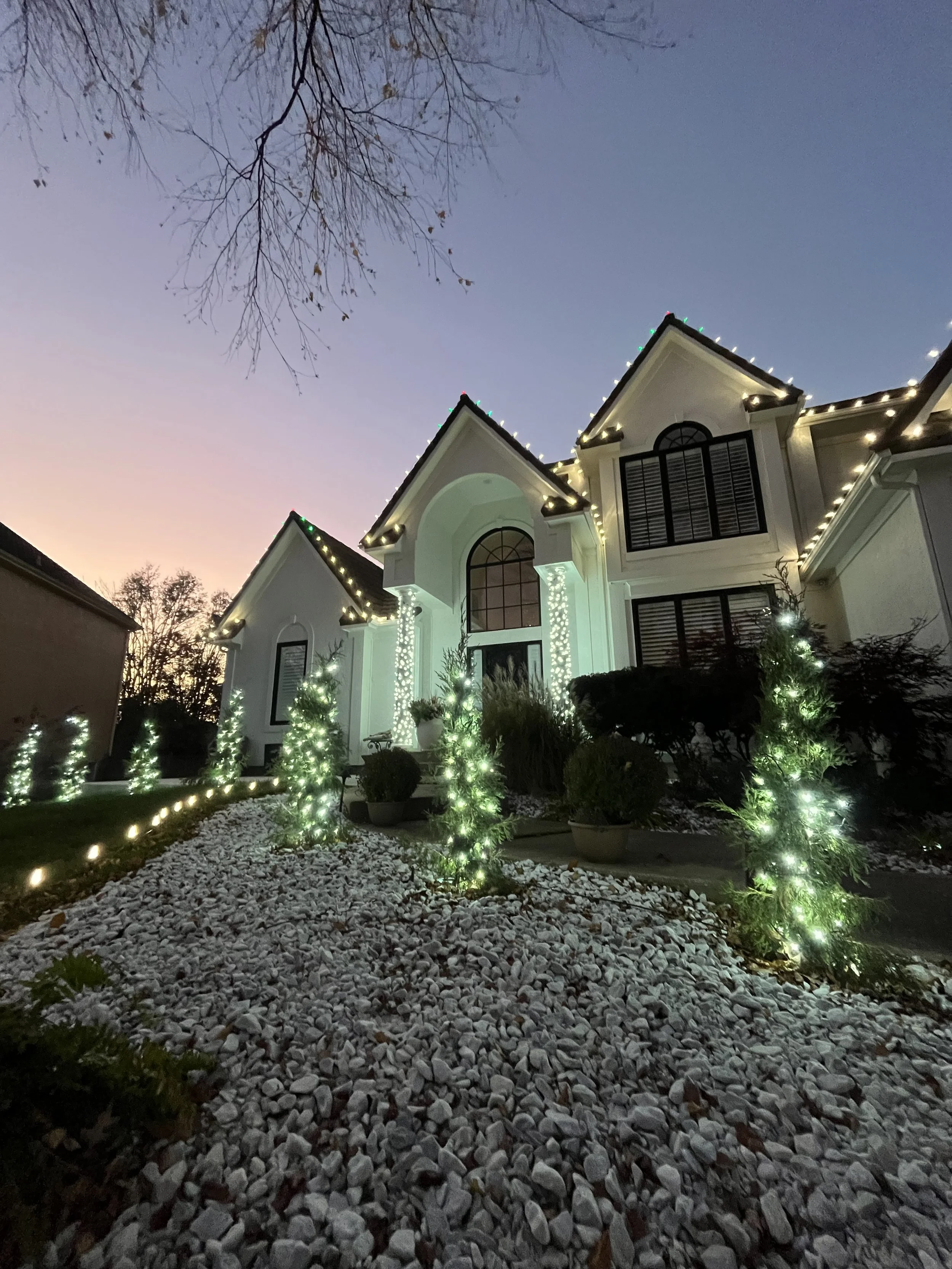 Large home with a beautiful Christmas lighting display including wrapped trees, ground lighting and roofline lighting