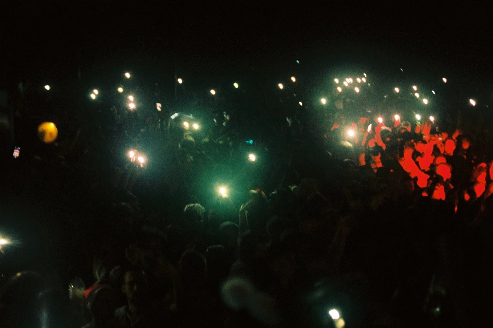analogue film photograph of massive illegal Halloween rave in Bristol during lockdown with crowd holding phone lights at night