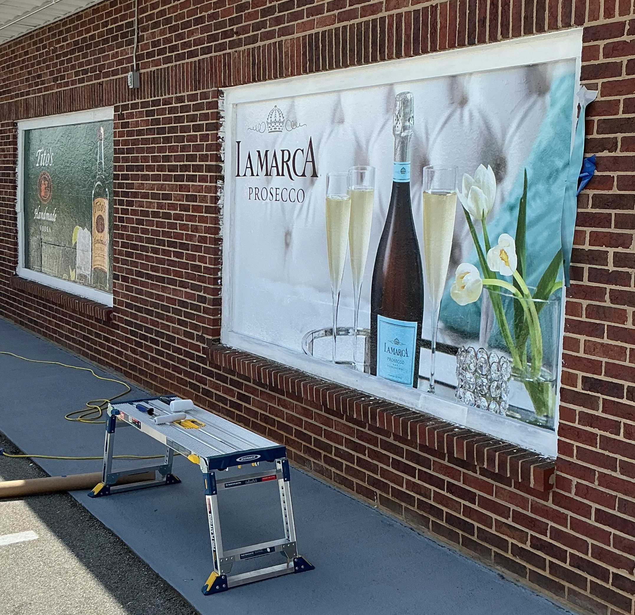 A ladder leaning against a brick wall outside of a building with signs advertising Prosecco and other products.