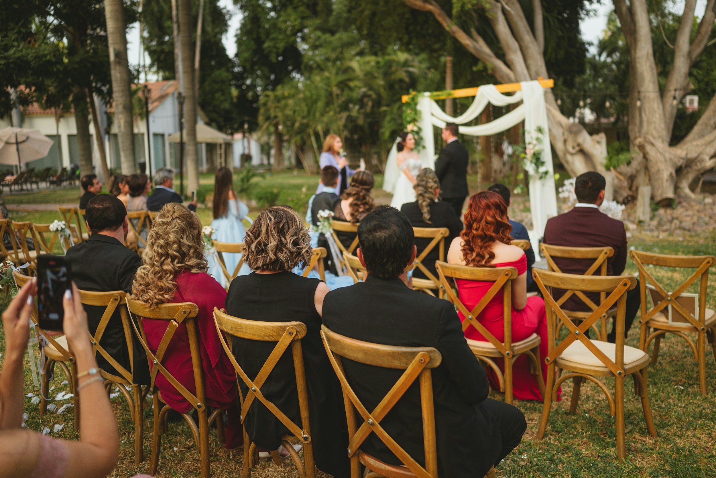 Friend leads an outdoor DIY wedding ceremony as guests watch and take pictures.