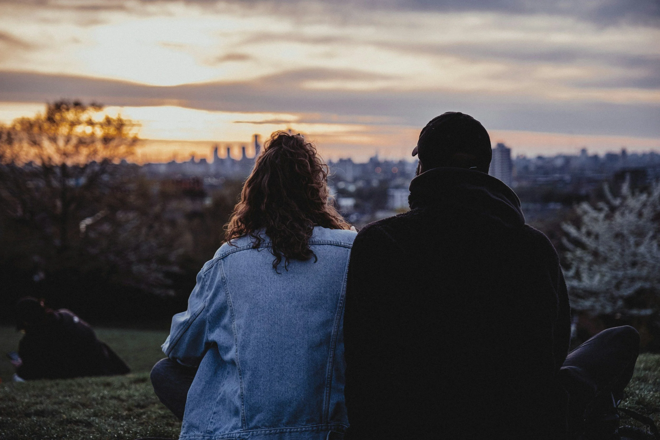A couple sit side by side overlooking the city at sunset