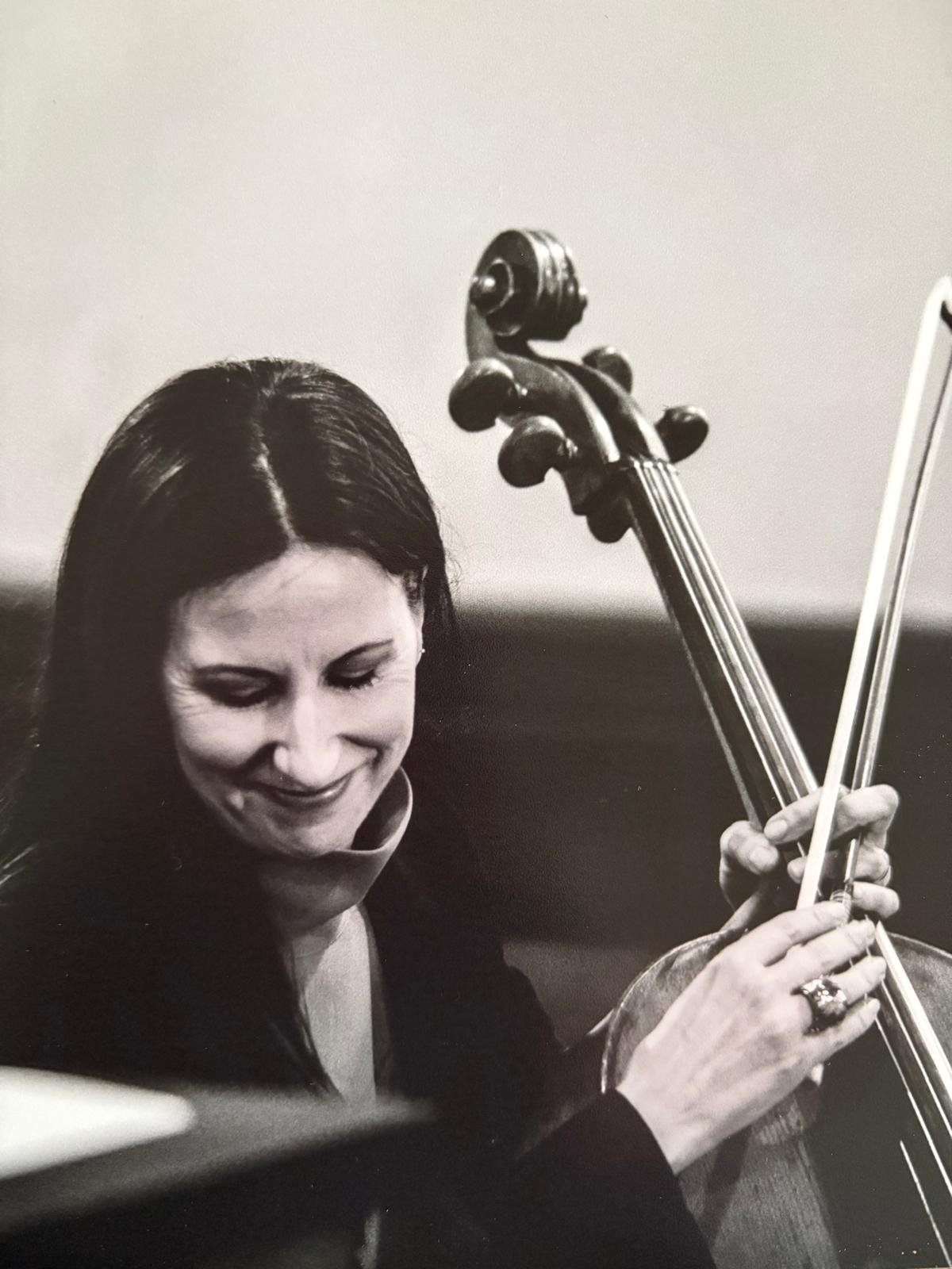 A black and white photo of Diana smiling while playing a cello.