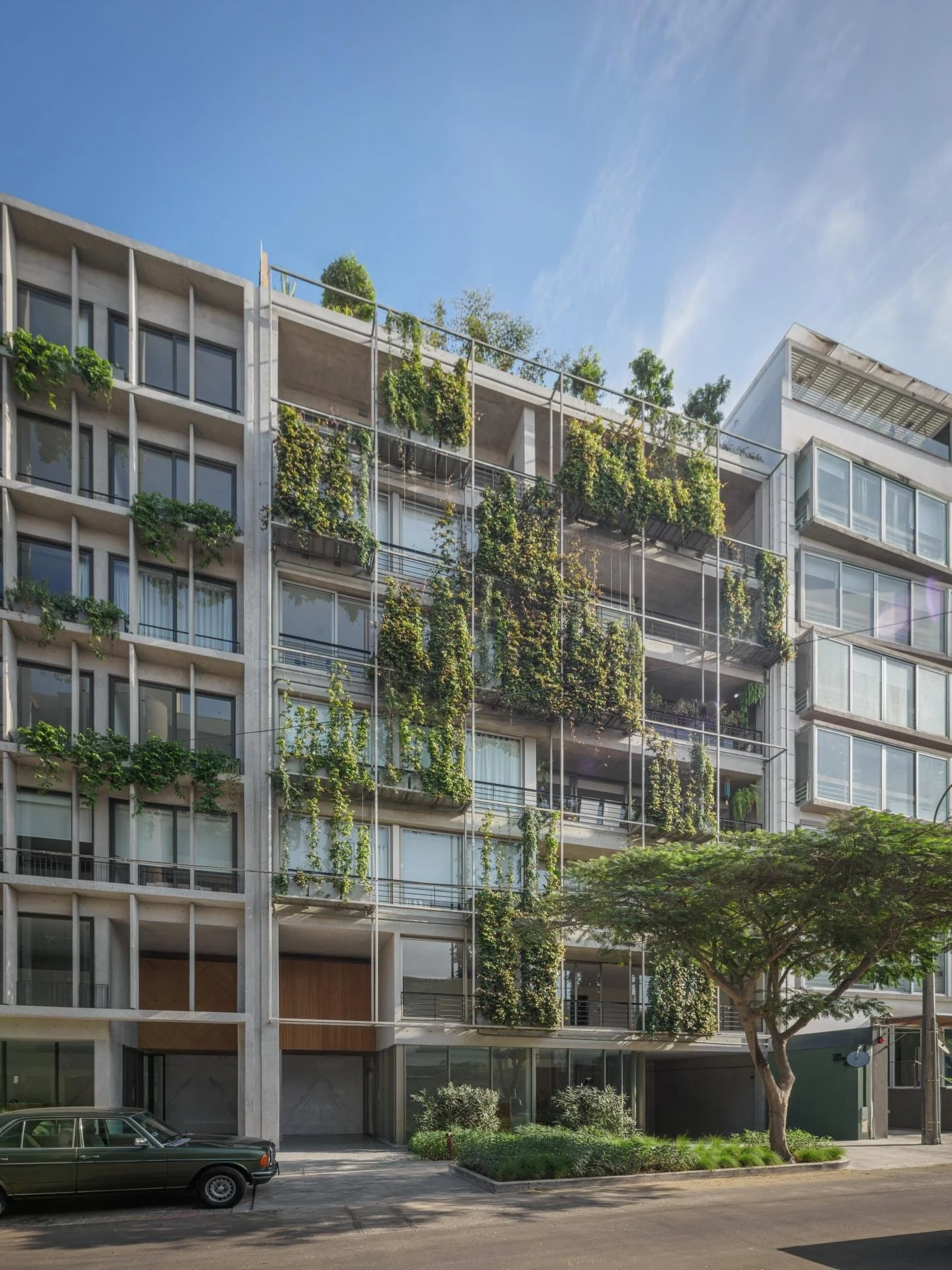 Edificio residencial con jardines en las terrazas y un árbol en la acera.