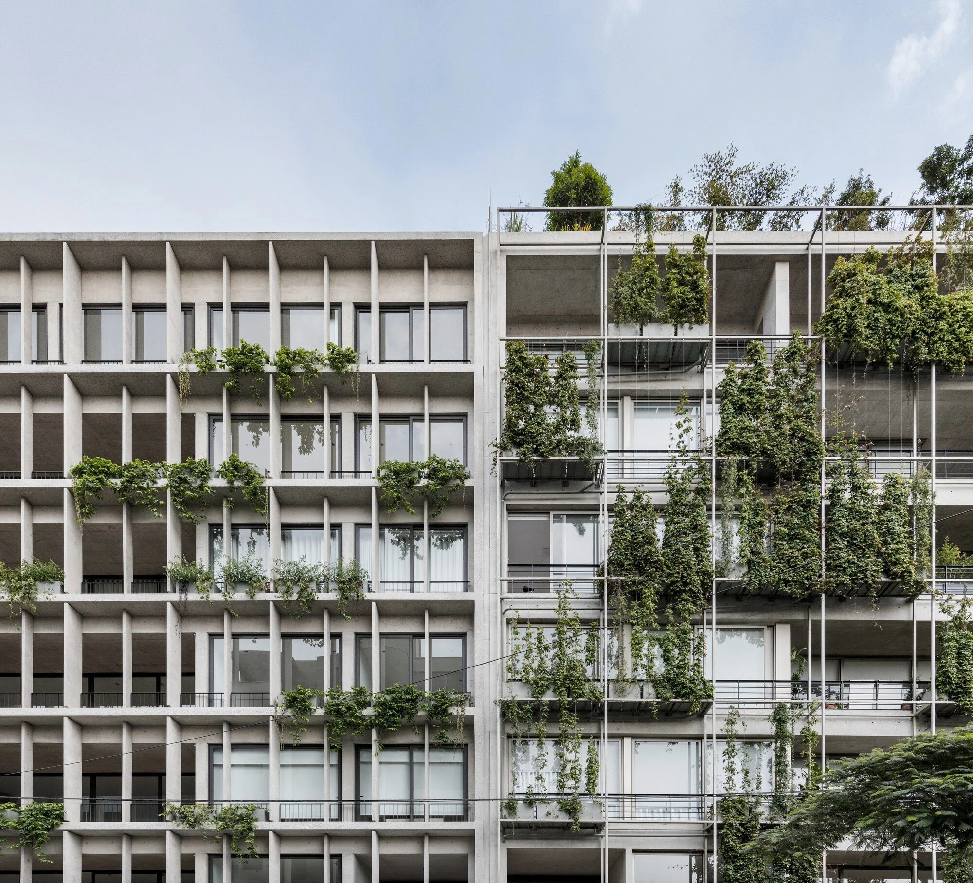 Edificio moderno con estructura de concreto y balcones con plantas verdes en cada piso.